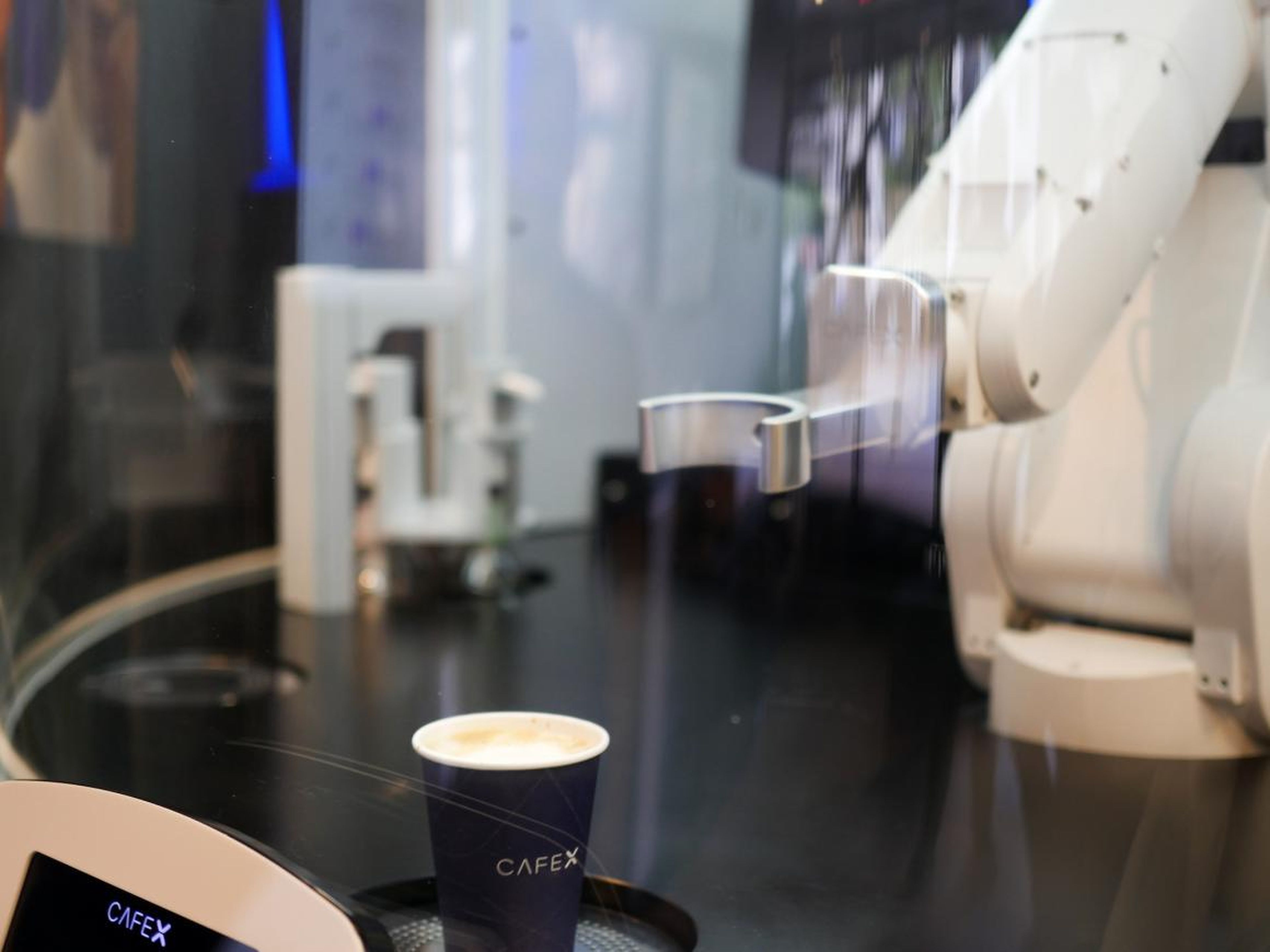 El brazo robot tras la barra de CafeX prepara un pedido de café para un cliente.