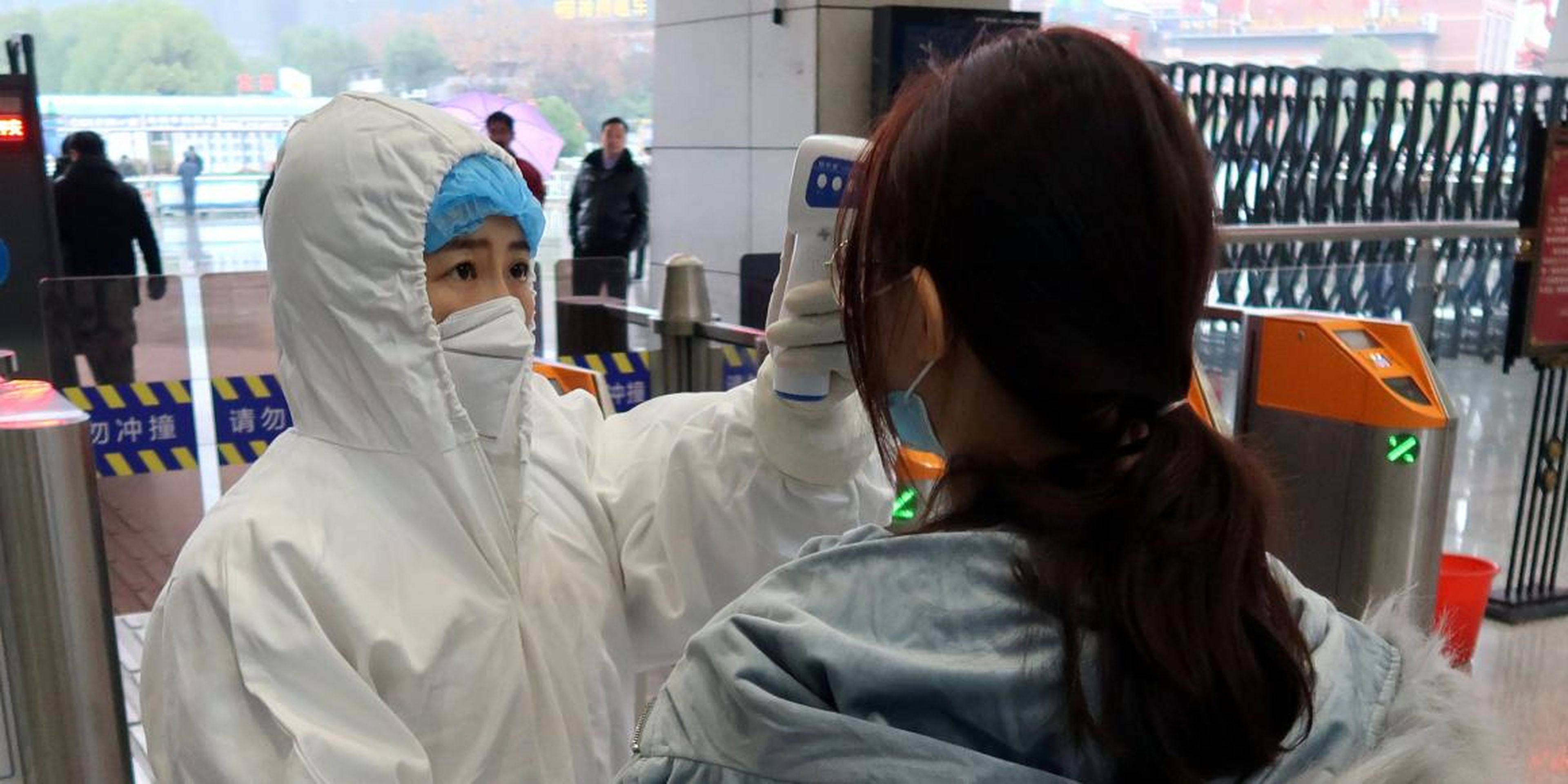 Un trabajador con traje protector controla la temperatura de pasajeros antes de entrar a una estación de Wuhan el 24 de enero de 2020.