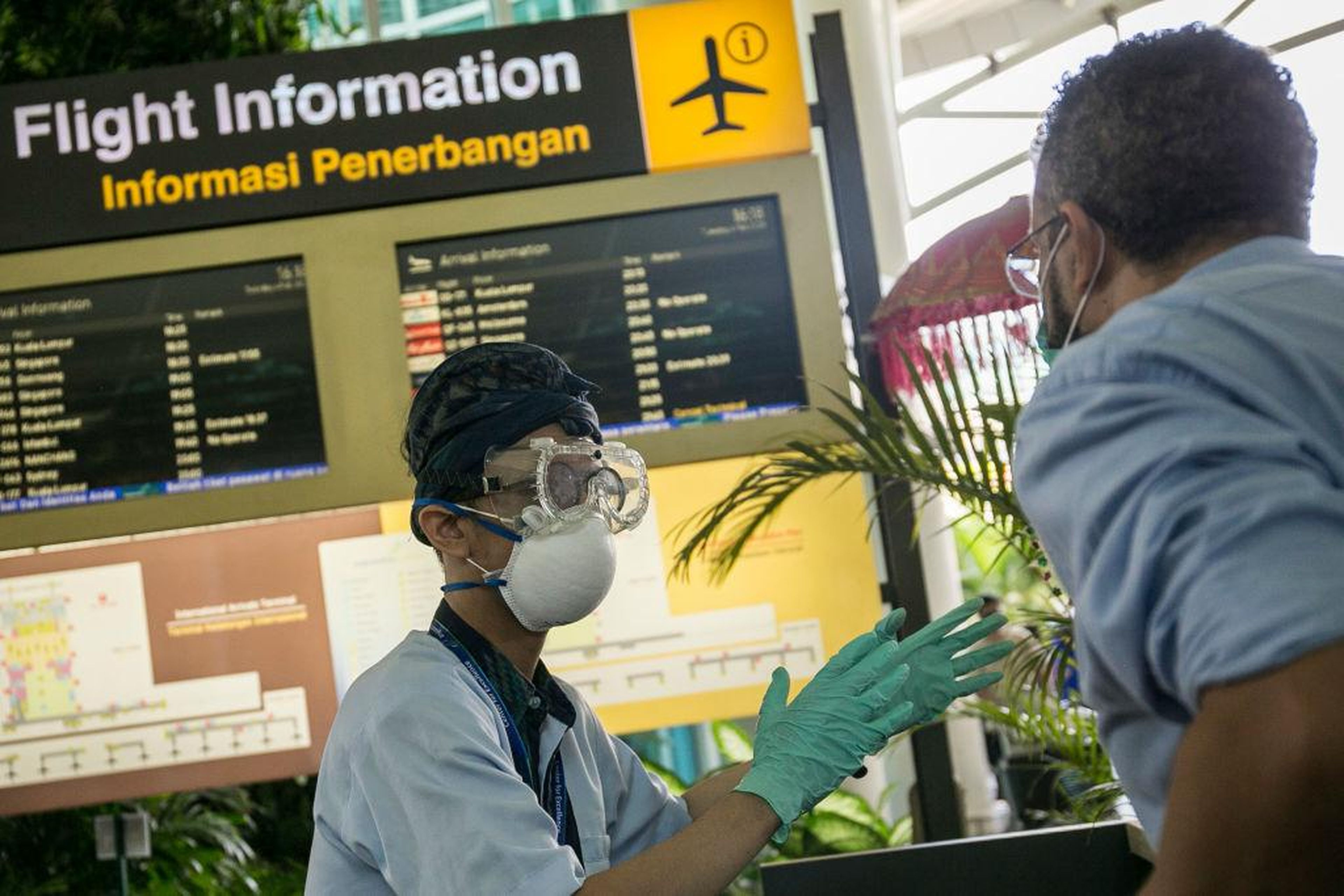 Information officer wearing protective mask, gloves and goggle, as prevention of novel coronavirus epidemic, gives directions to a passenger at international arrival gate of Bali Ngurah Rai International Airport in Kuta, Bali, Indonesia on February 4 2020
