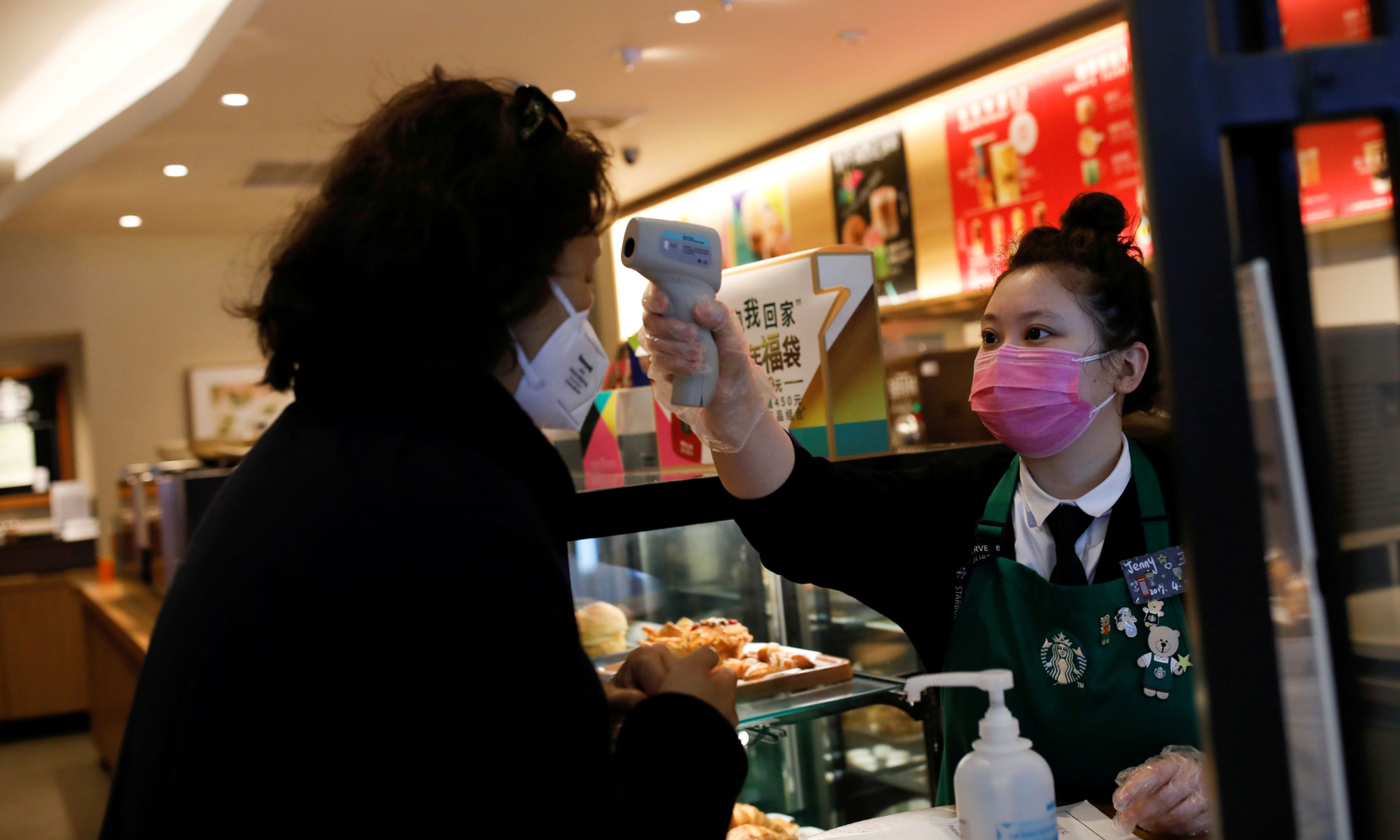 Una camarera mide la temperatura de una clienta en una cafetería Starbucks en Pekín