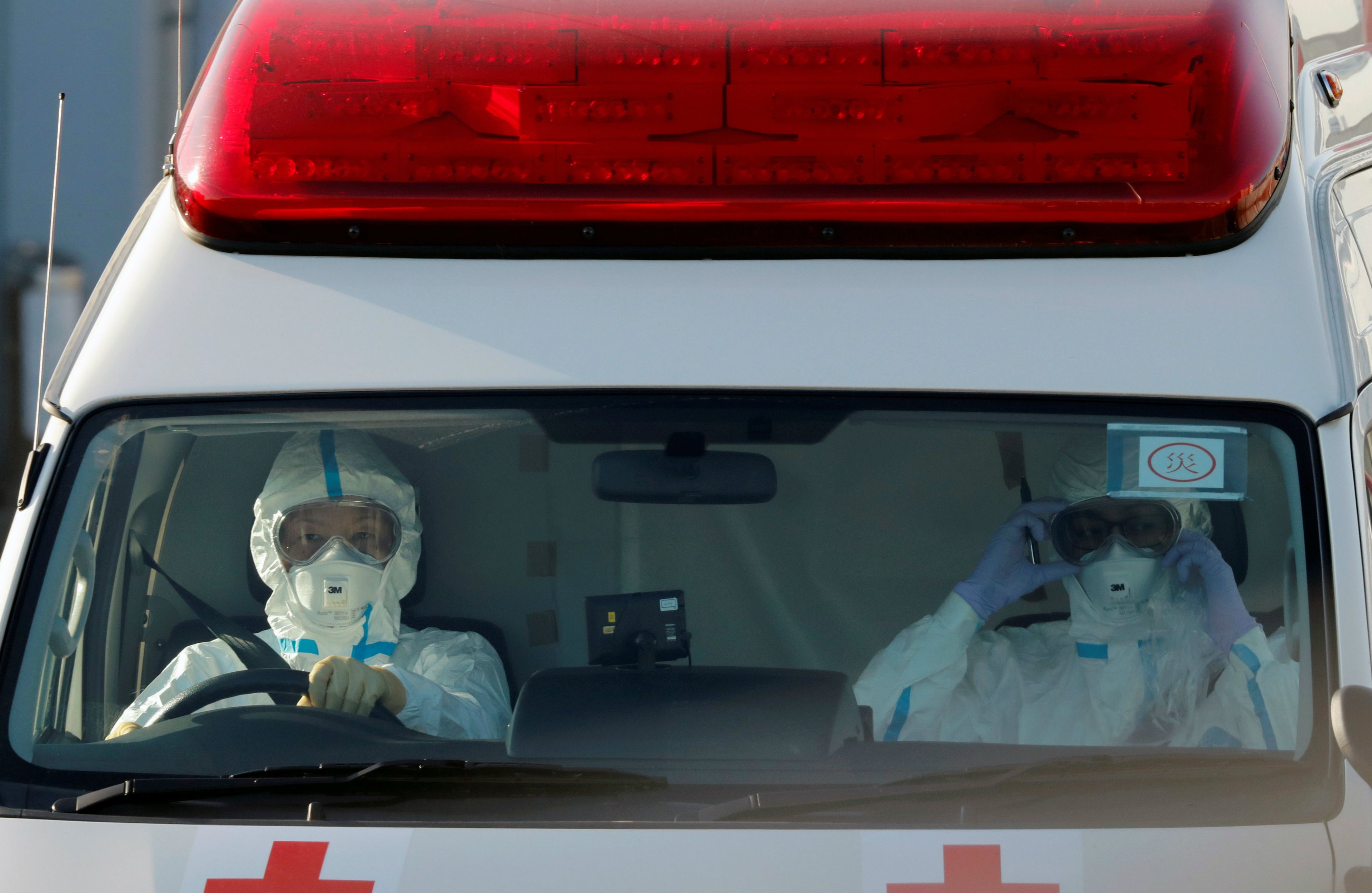 Conductores de una ambulancia llevan trajes protectores para transferir a los viajeros del Diamond Princess que han dado positivo del coronavirus.