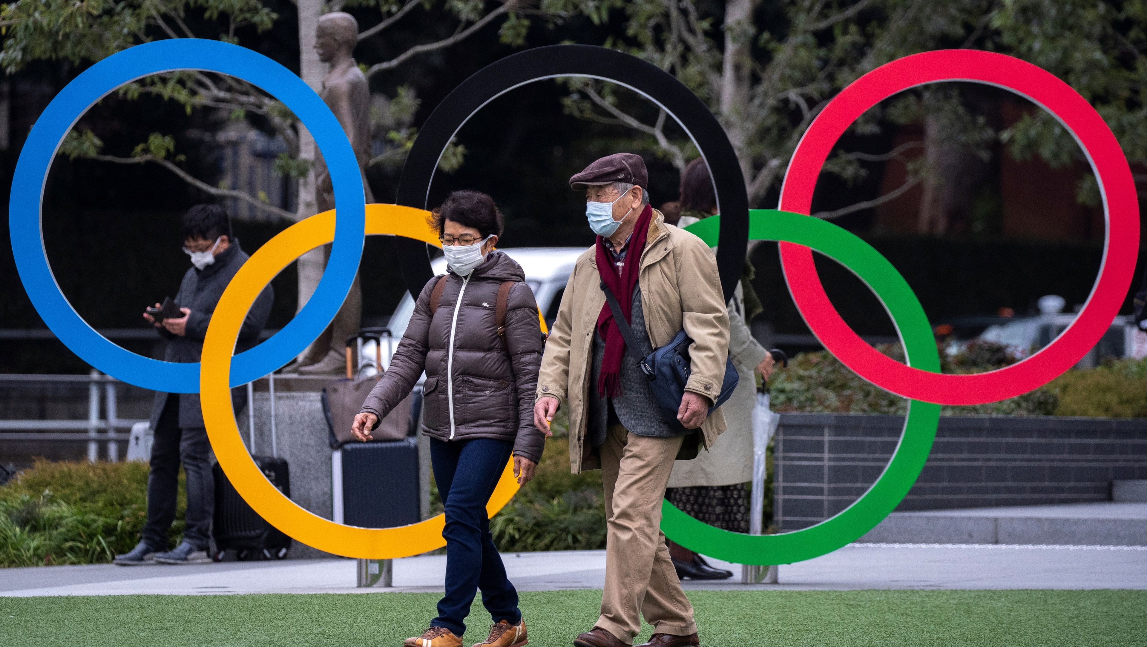 Dos japoneses caminan frente al logo de los Juegos Olímpicos de Tokio en pleno brote por el coronavirus.