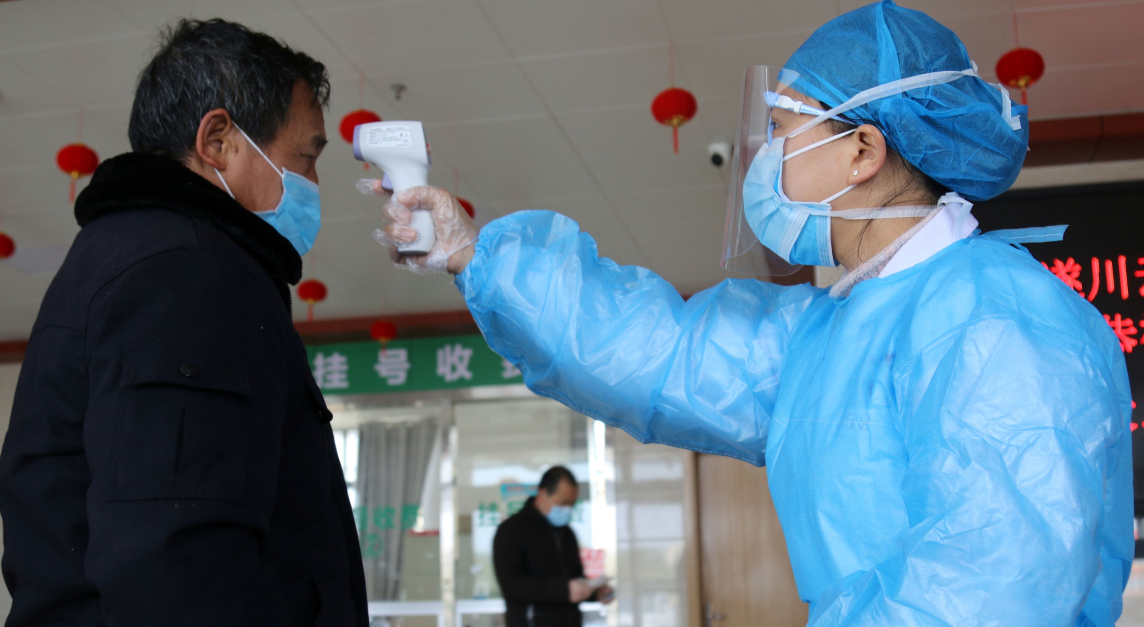 Una funcionaria toma la temperatura a un hombre a la entrada de un edificio público en Sichuan (China)
