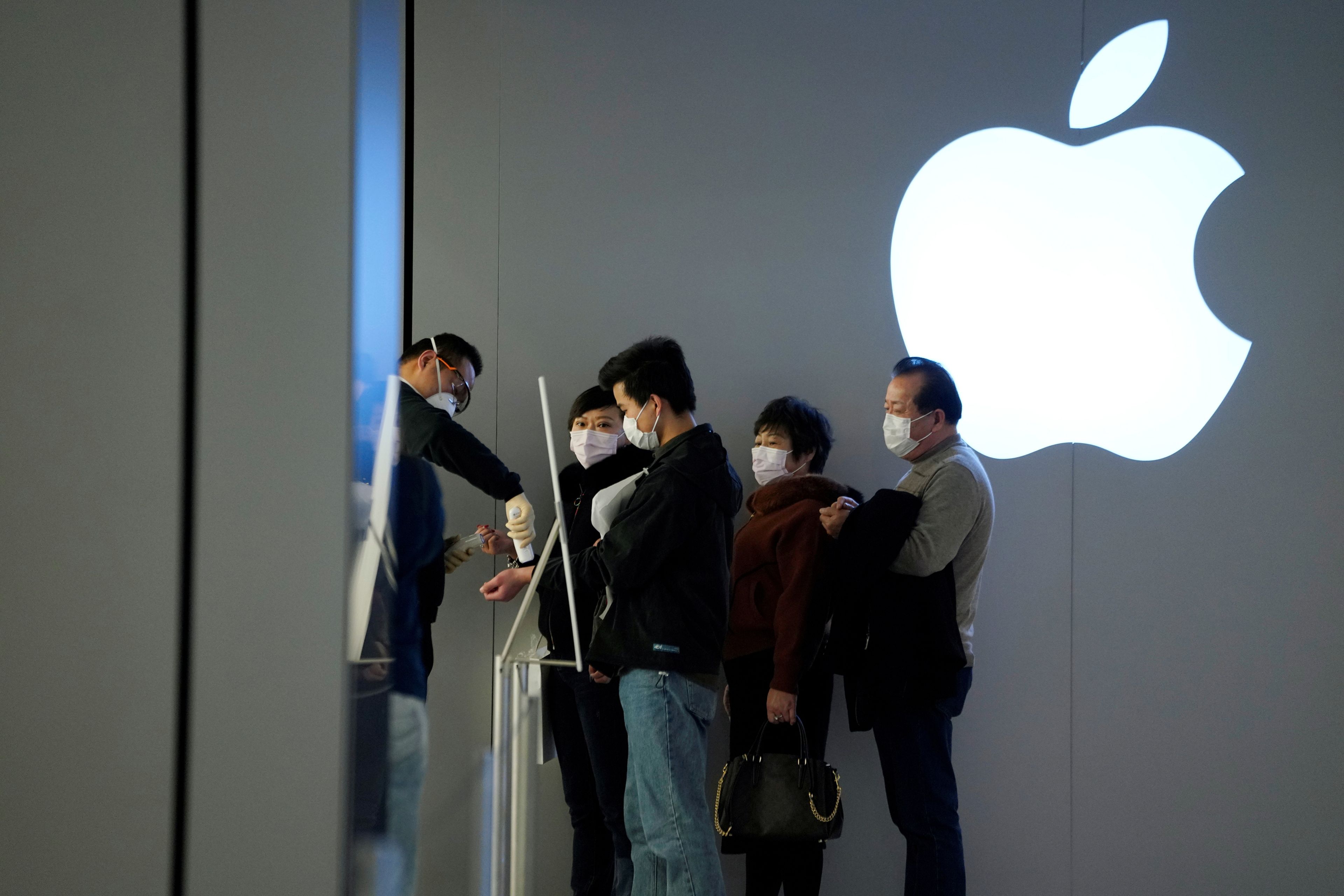 Un grupo de personas equipadas con máscaras protectoras esperan a pasar un test de temperatura antes de entrar a una Apple Store en Shanghái.