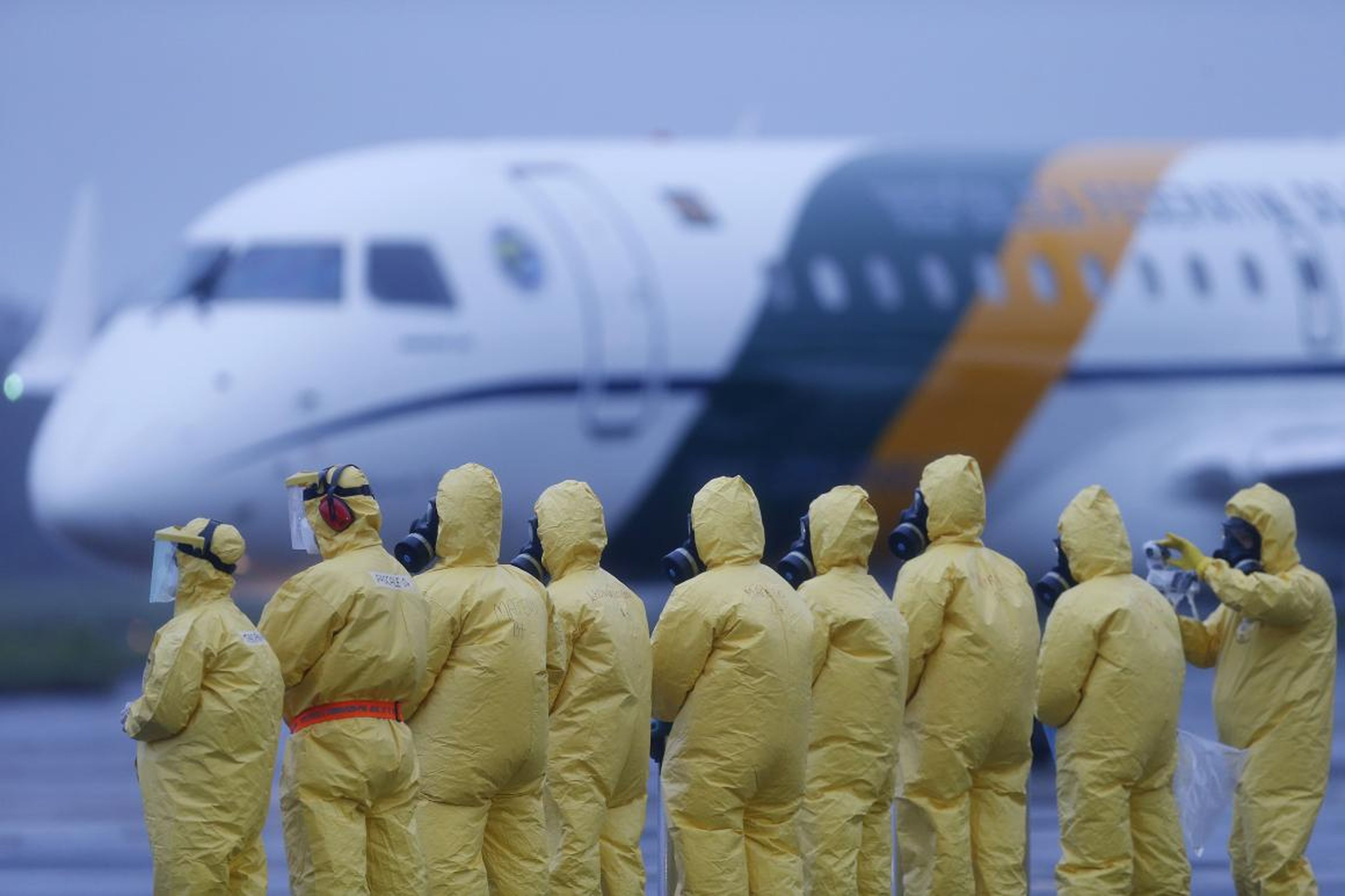 Soldados con trajes protectores esperan a pasajeros repatriados desde Wuhan, China.