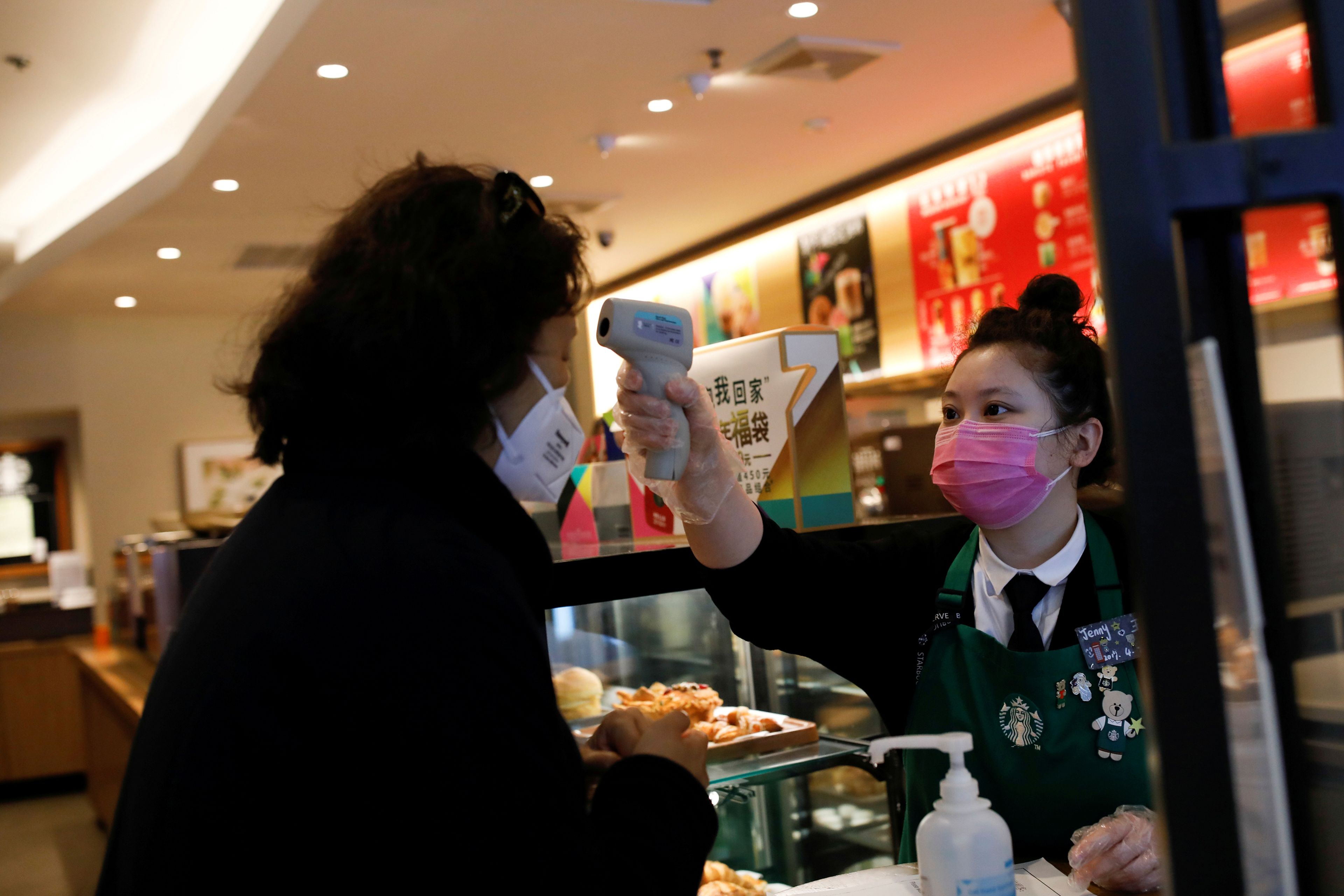 Una trabajadora de un Starbucks en Pekín utiliza un termómetro para medir la temperatura de un cliente en medio del brote del coronavirus.