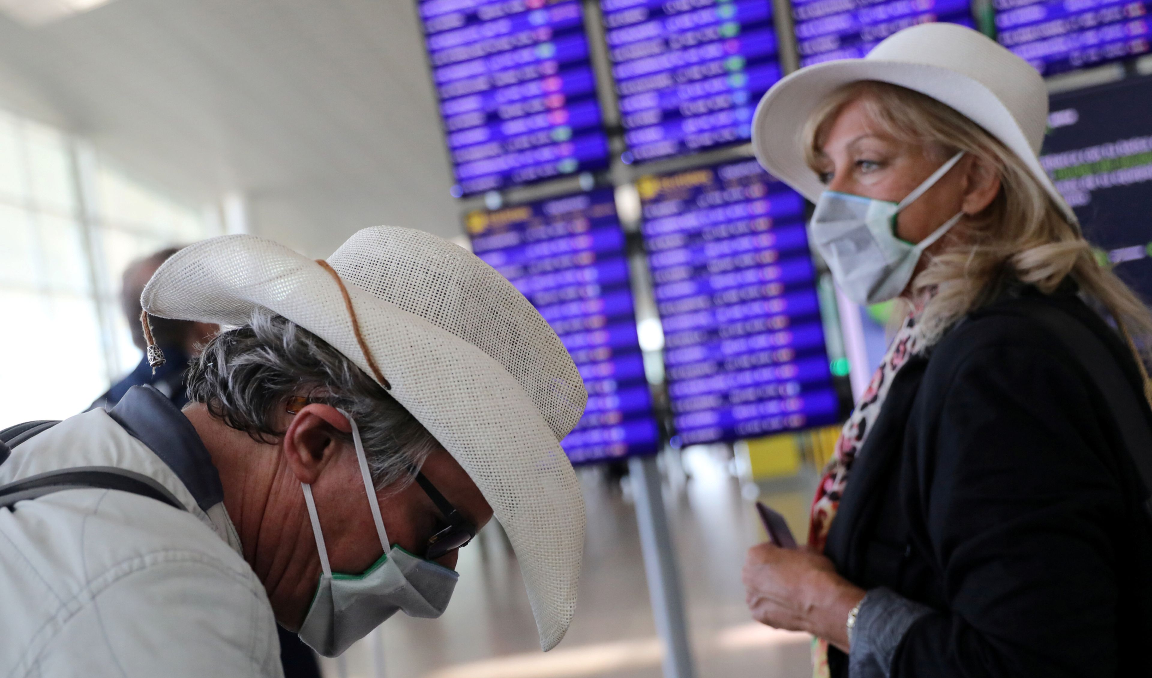Unos turistas con mascarilla esperan información de vuelo en el aeropuerto de El Prat