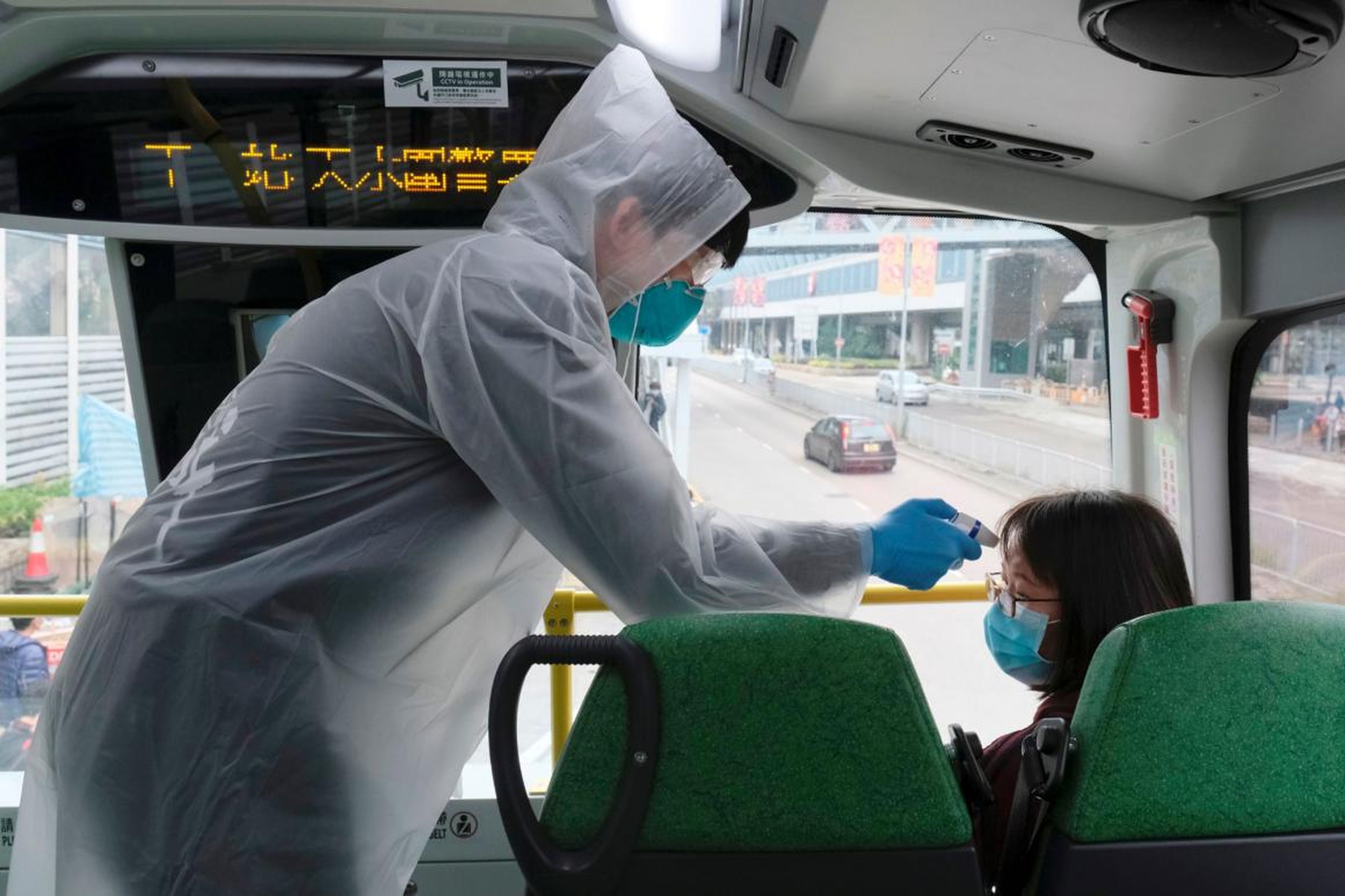 A resident wearing mask and raincoat takes the temperature of passenger at a bus stop at Tin Shui Wai, China, February 4, 2020.