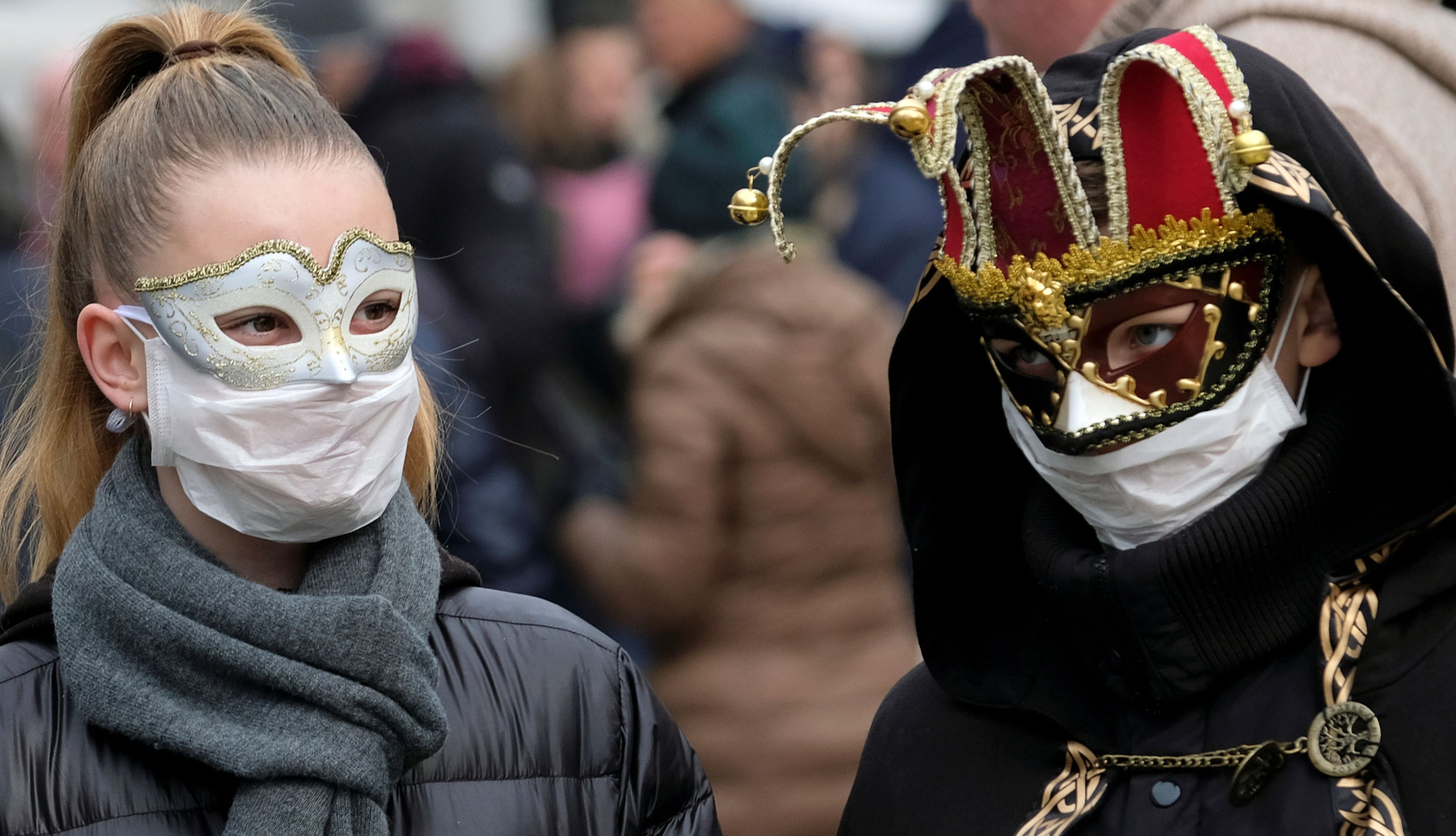 2 asistentes al Carnaval de Venecia con mascarillas sanitarias debajo de sus máscaras