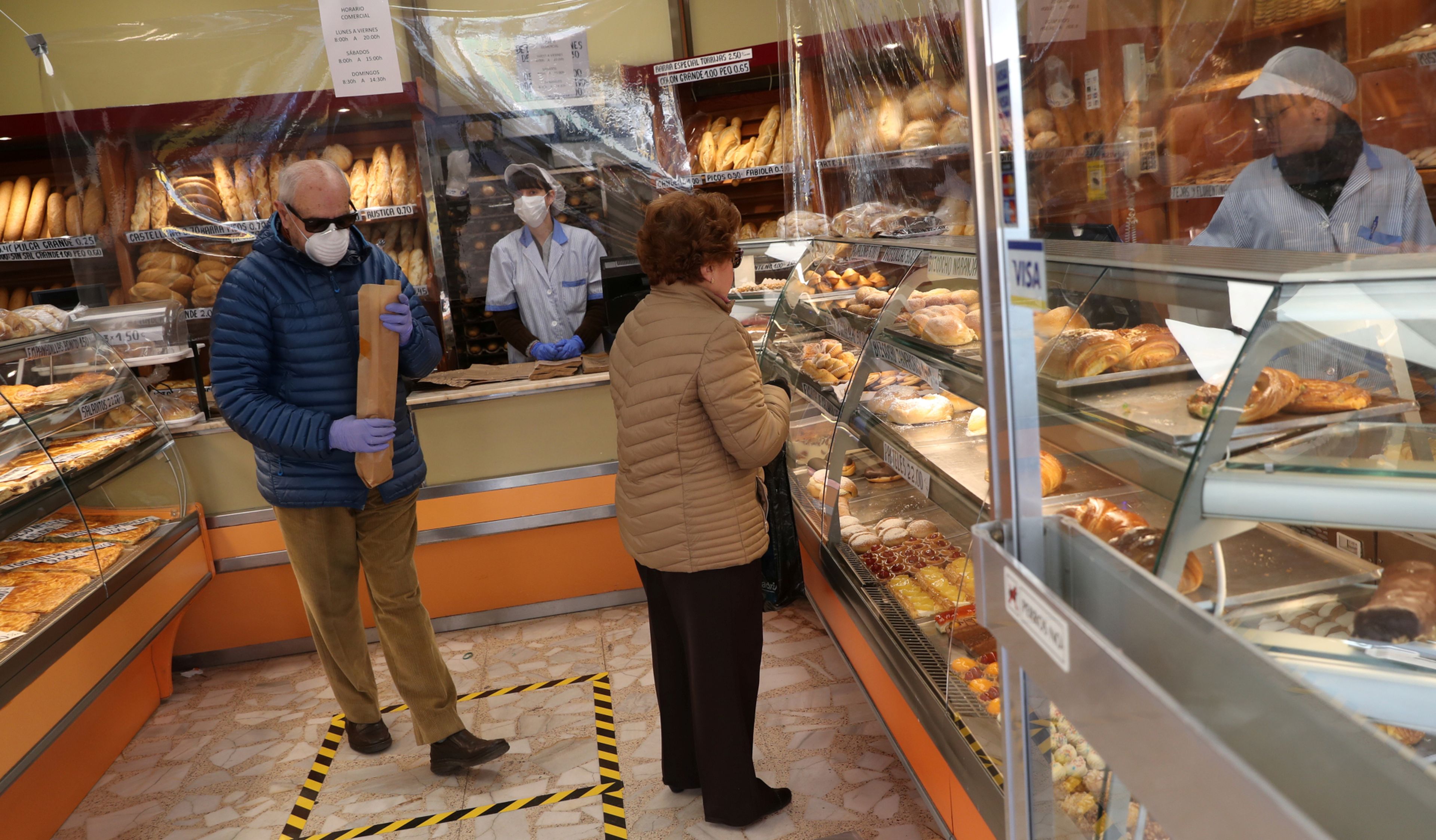 2 clientes con mascarilla compran pan en una panadería de Madrid