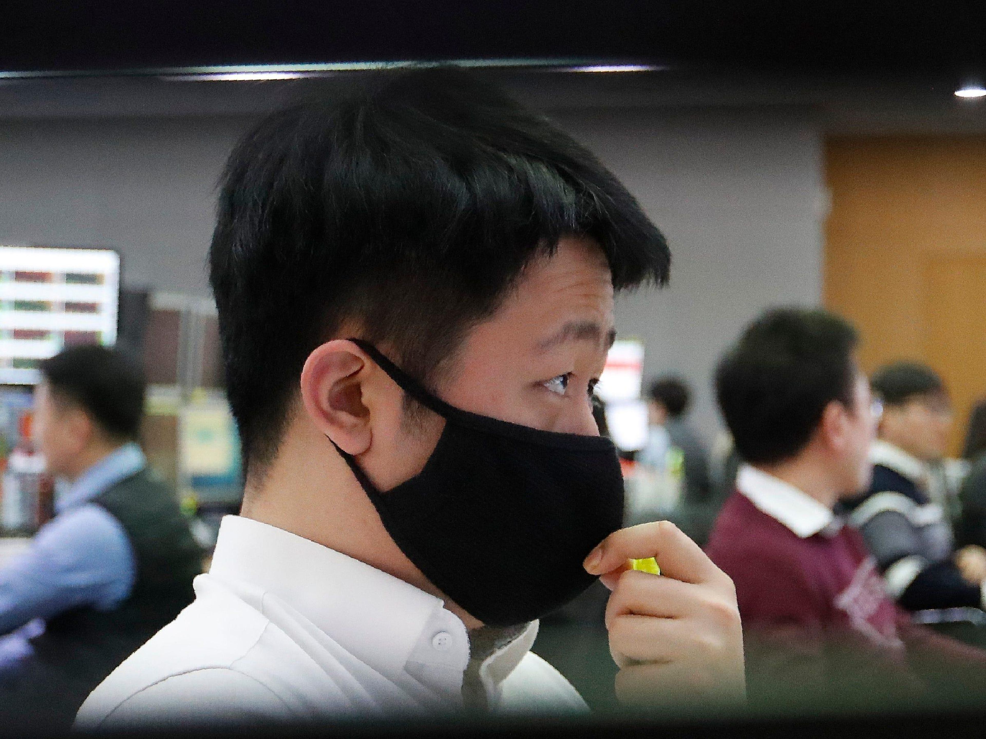 Un comerciante de divisas con una mascarilla observa los monitores en la sala de comercio de divisas.