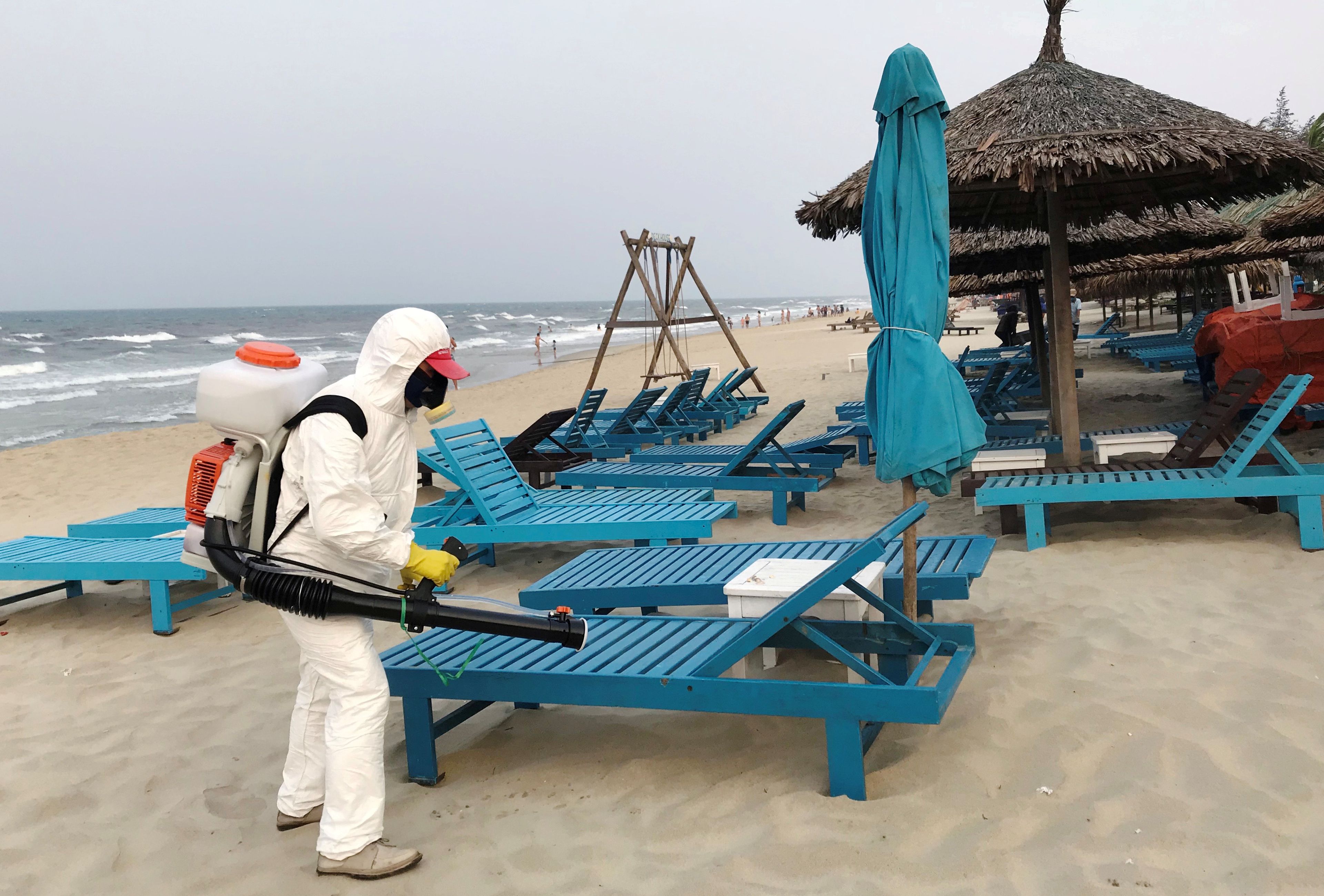 Un hombre con traje de protección desinfecta unas tumbonas de playa por el coronavirus.