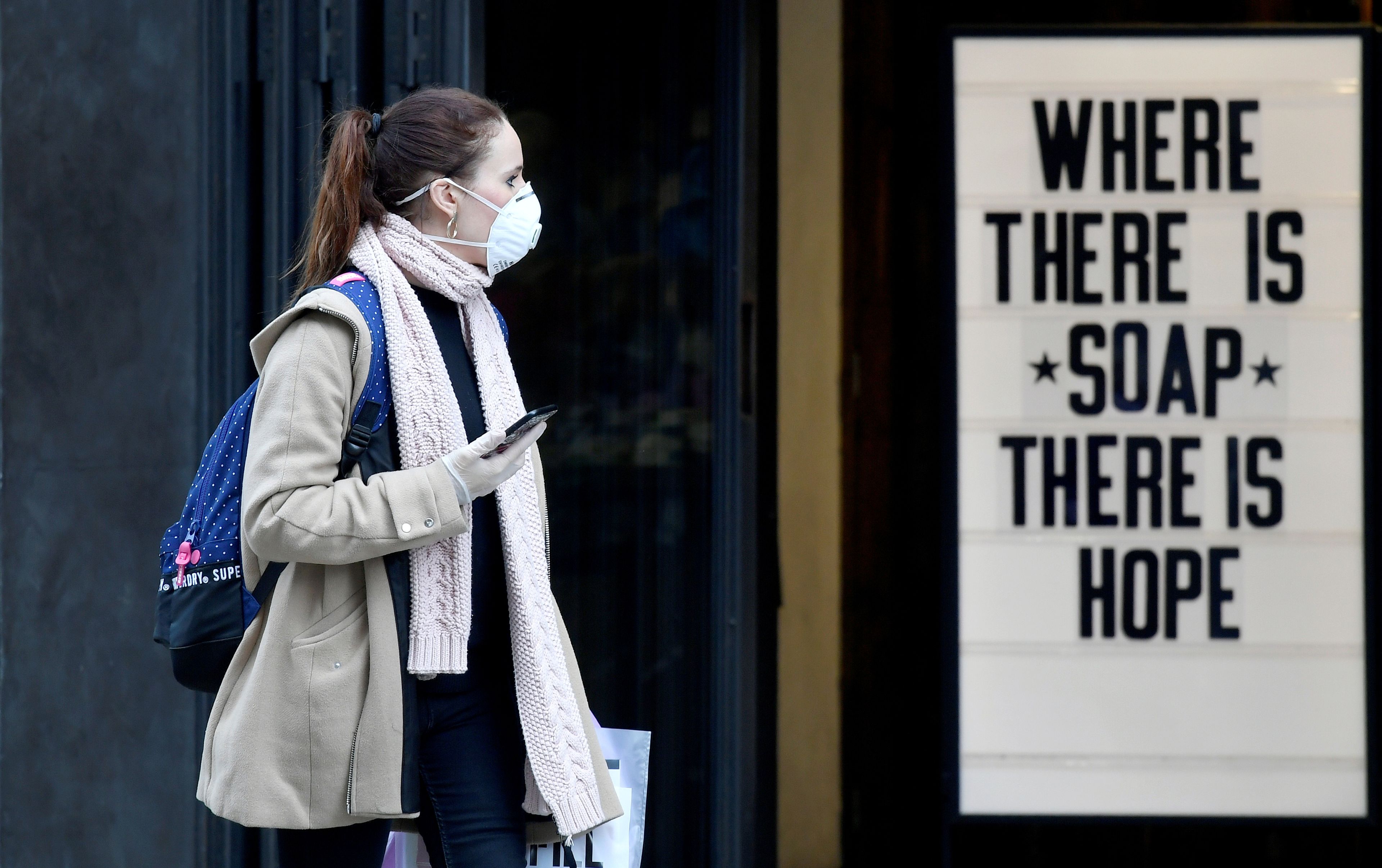 Una mujer con mascarilla pasa por delante de un cartel en la crisis del coronavirus.