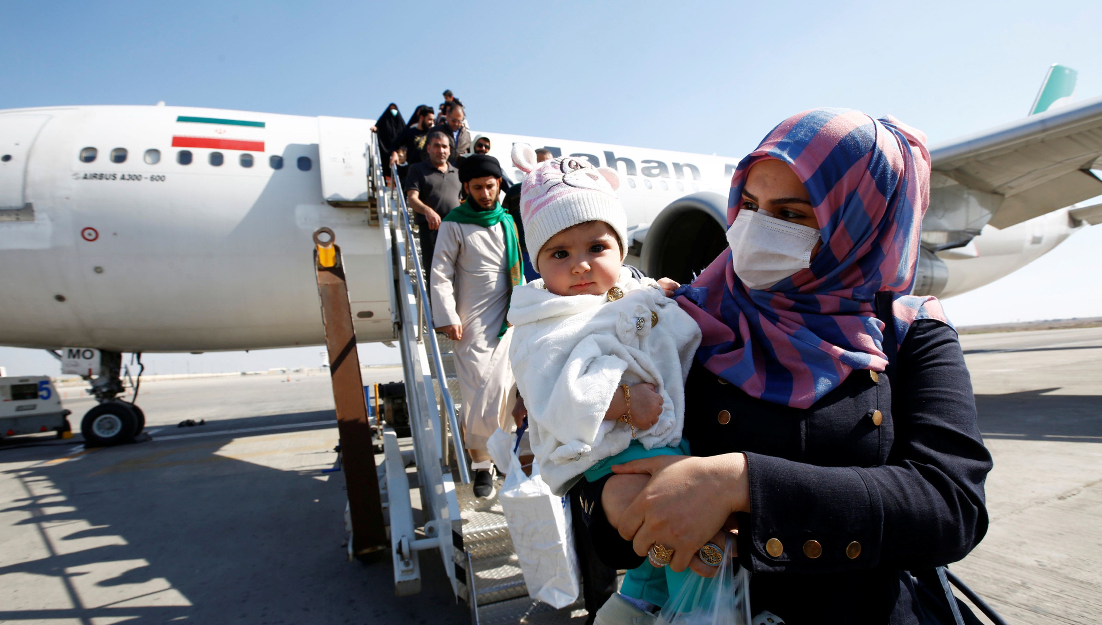 Pasajeros con mascarillas protectoras descienden de un avión en el aeropuerto de Najaf (Irán)