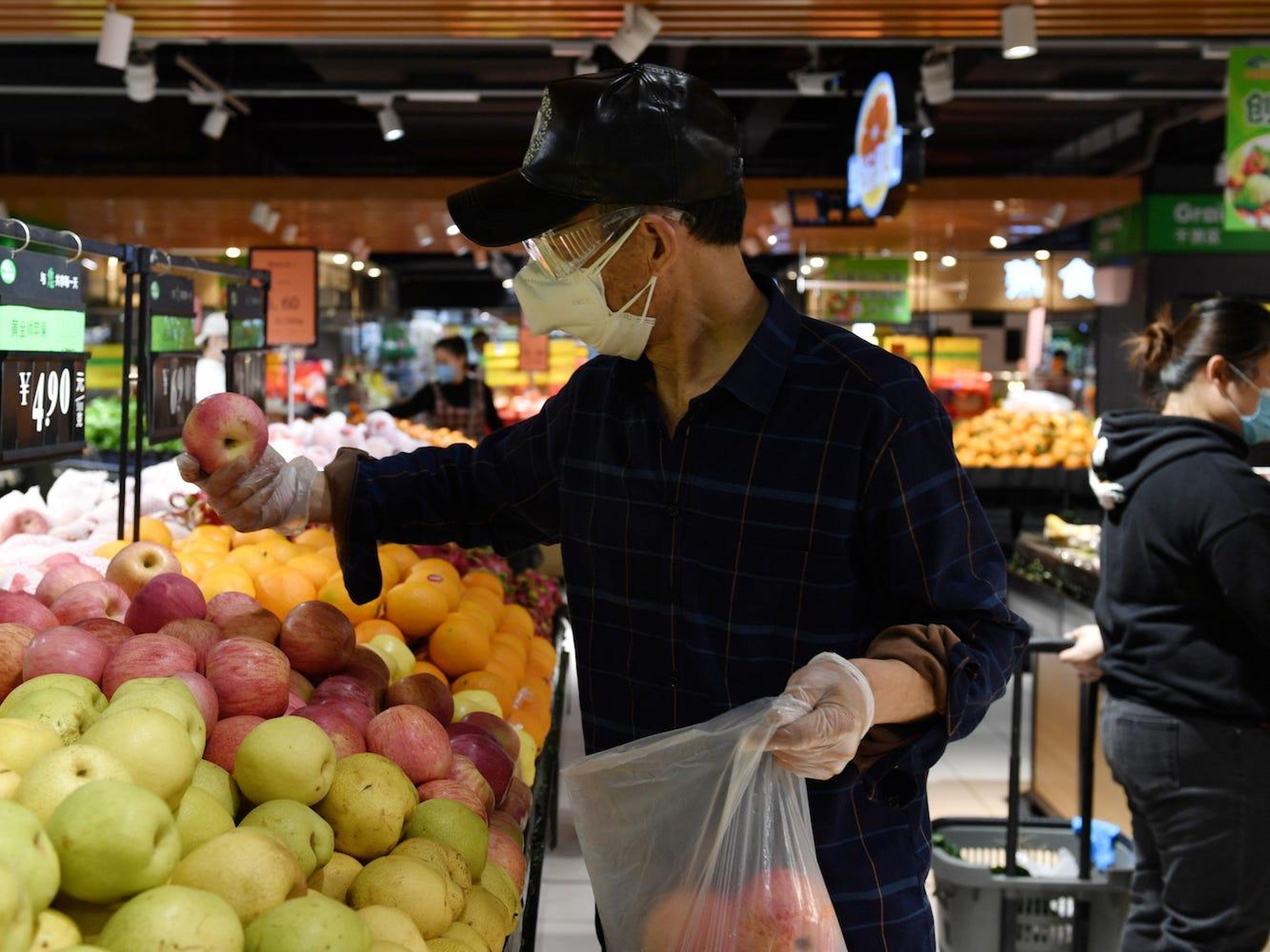 Un hombre con mascarilla y gafas coge manzanas dentro de un supermercado en Wuhan, provincia de Hubei, el 26 de marzo de 2020.