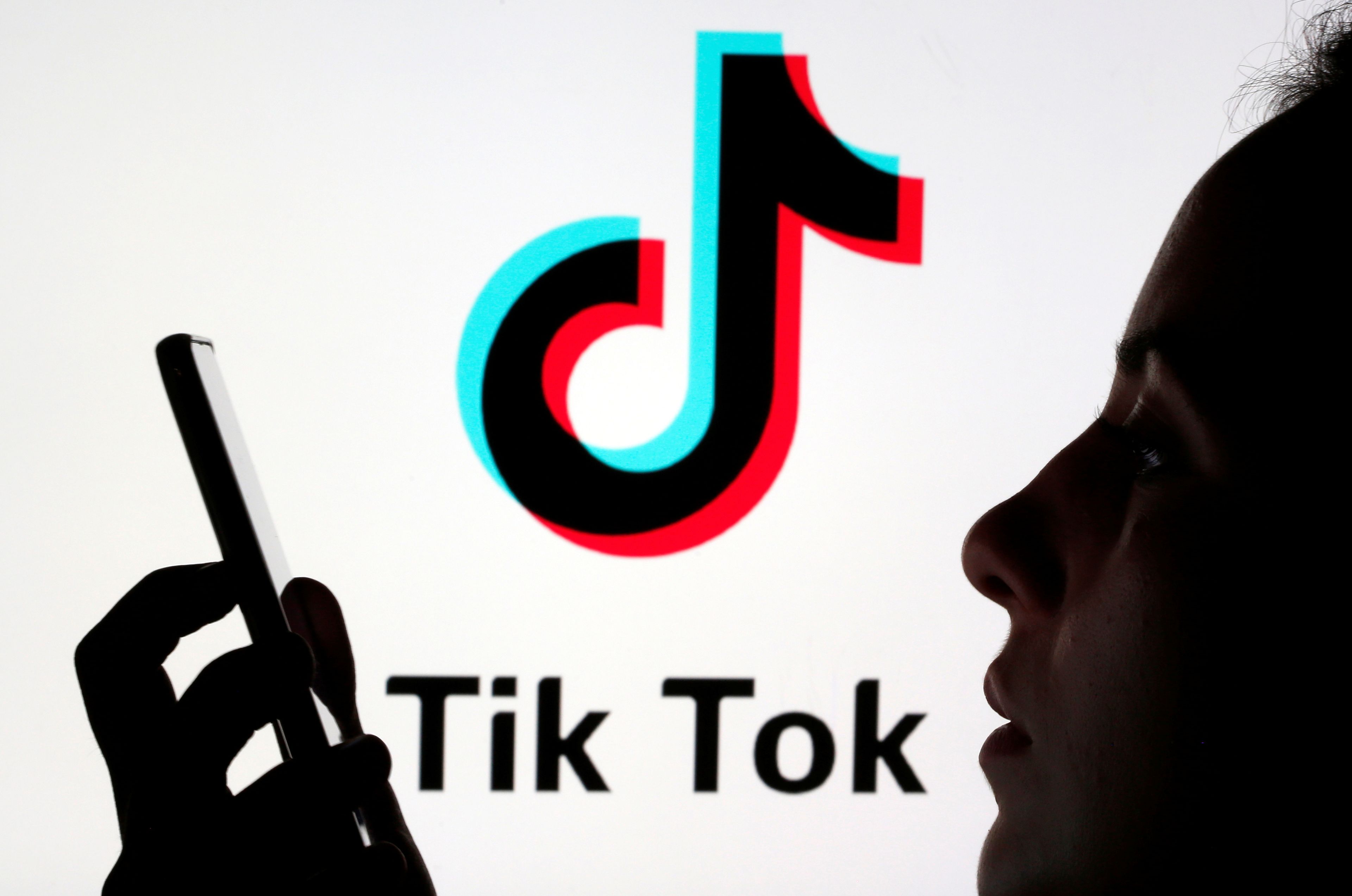 Una persona mira un móvil delante del logo deTik Tok