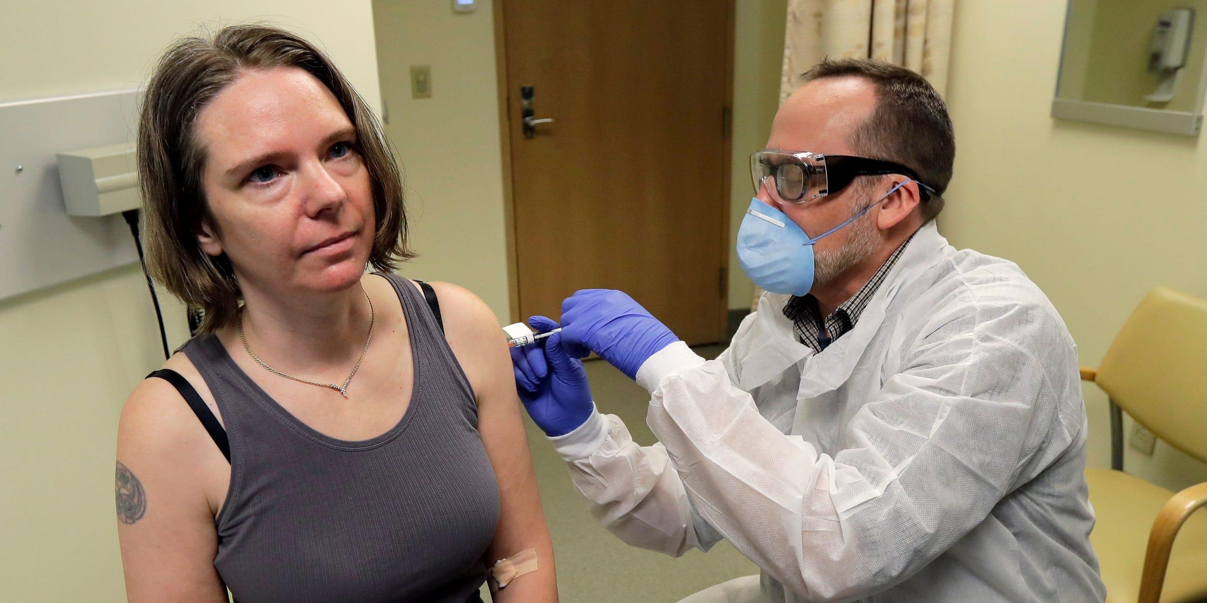 Un farmacéutico le da a Jennifer Haller, izquierda, la primera inyección de la primera etapa del estudio de seguridad de una posible vacuna para COVID-19, la enfermedad causada por el nuevo coronavirus.