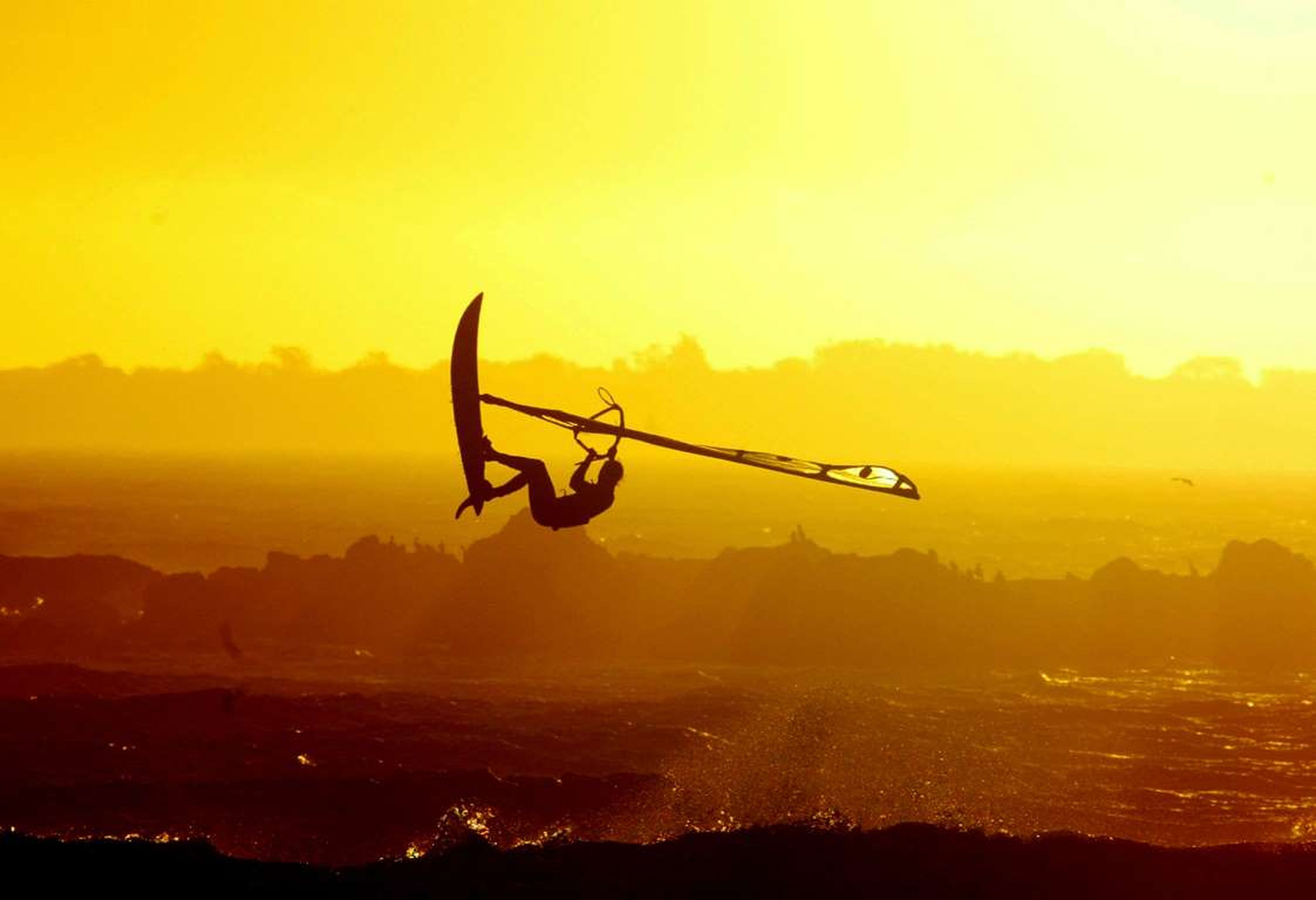 Un surfista hace una acrobacia durante la puesta de sol, en la playa de Blaauwberg, en la Ciudad del Cabo.