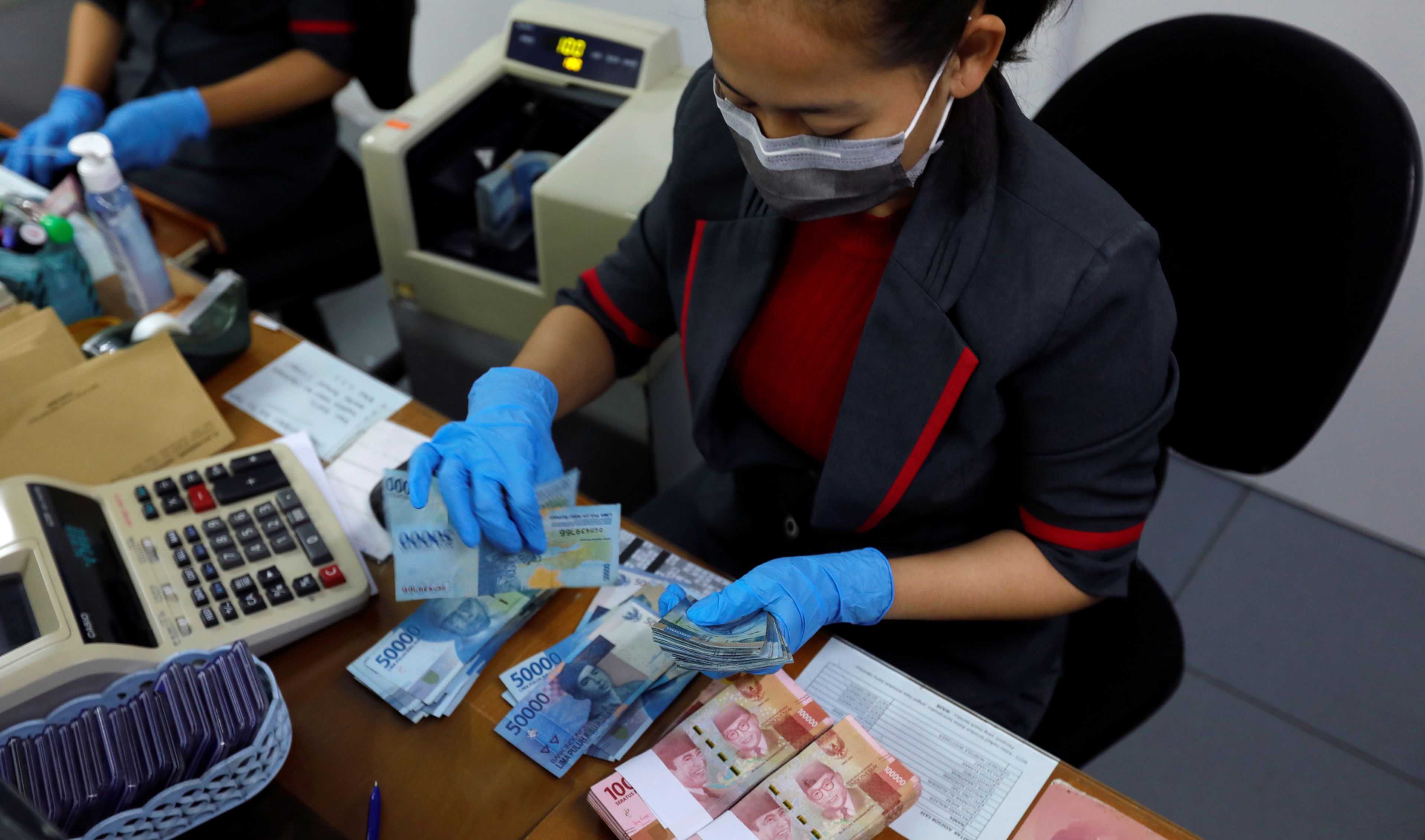 Una trabajadora del Banco Central de Indonesia cuenta billetes antes de su desinfección de coronavirus