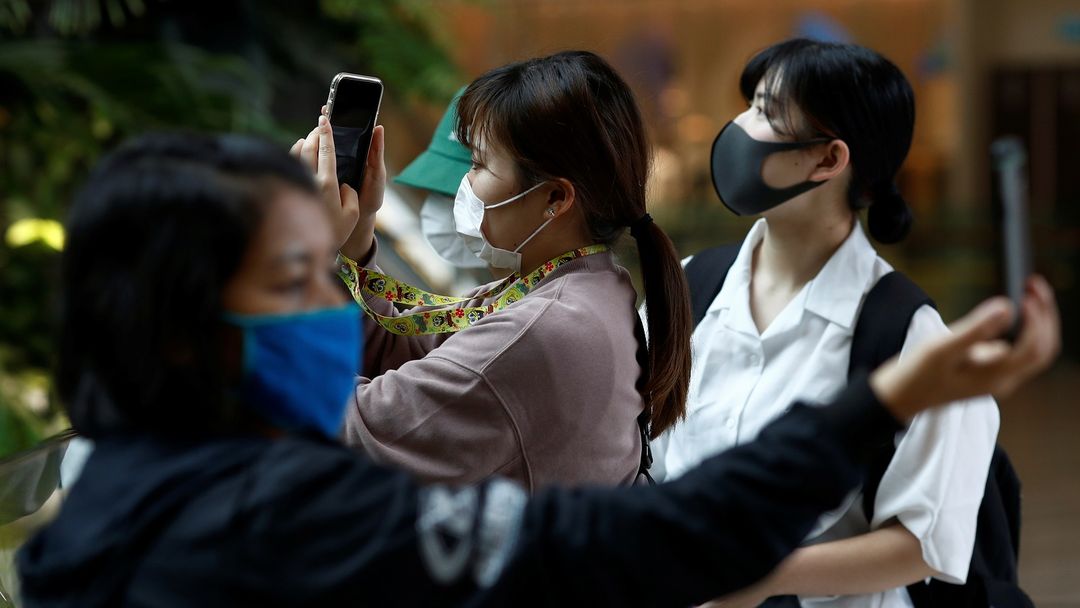 Tres turistas con mascarillas se sacan fotos durante el brote de coronavirus.