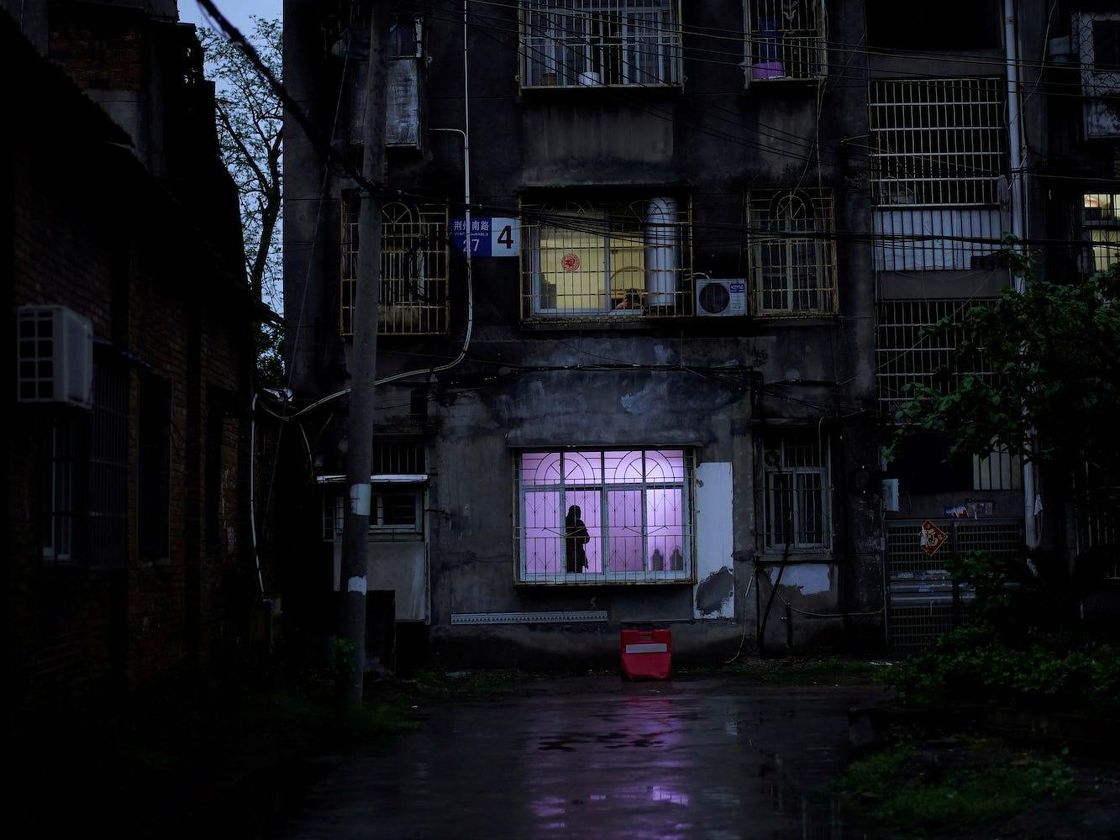 Un hombre se para frente a una ventana en una comunidad residencial en Jingzhou, el 26 de marzo de 2020.