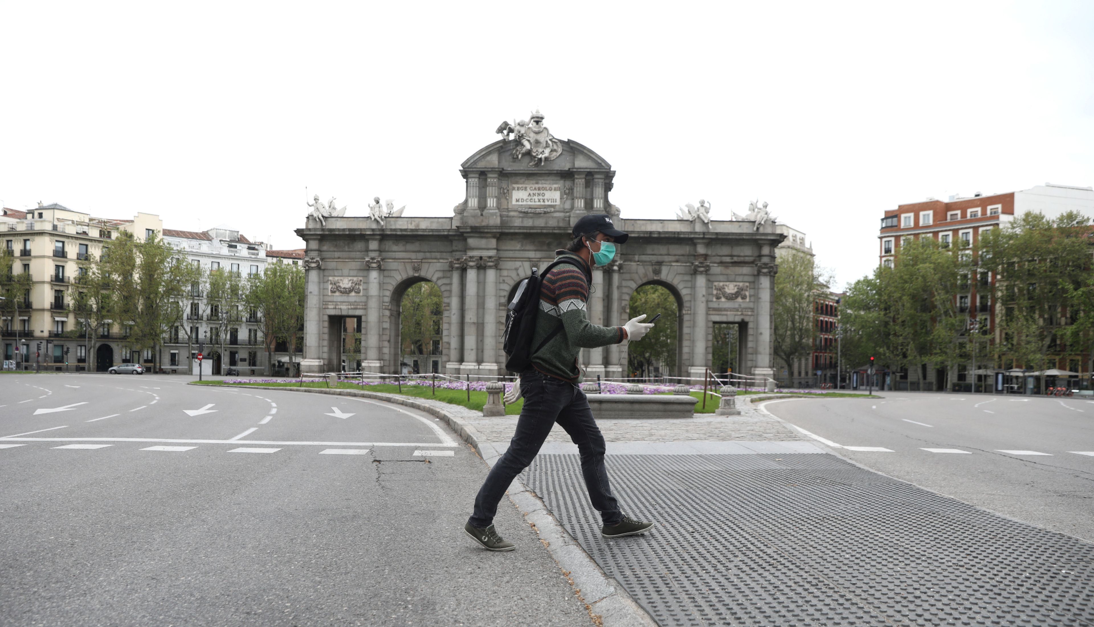 Un hombre cruza la calle con una mascarilla puesta ante la Puerta de Alcalá de Madrid