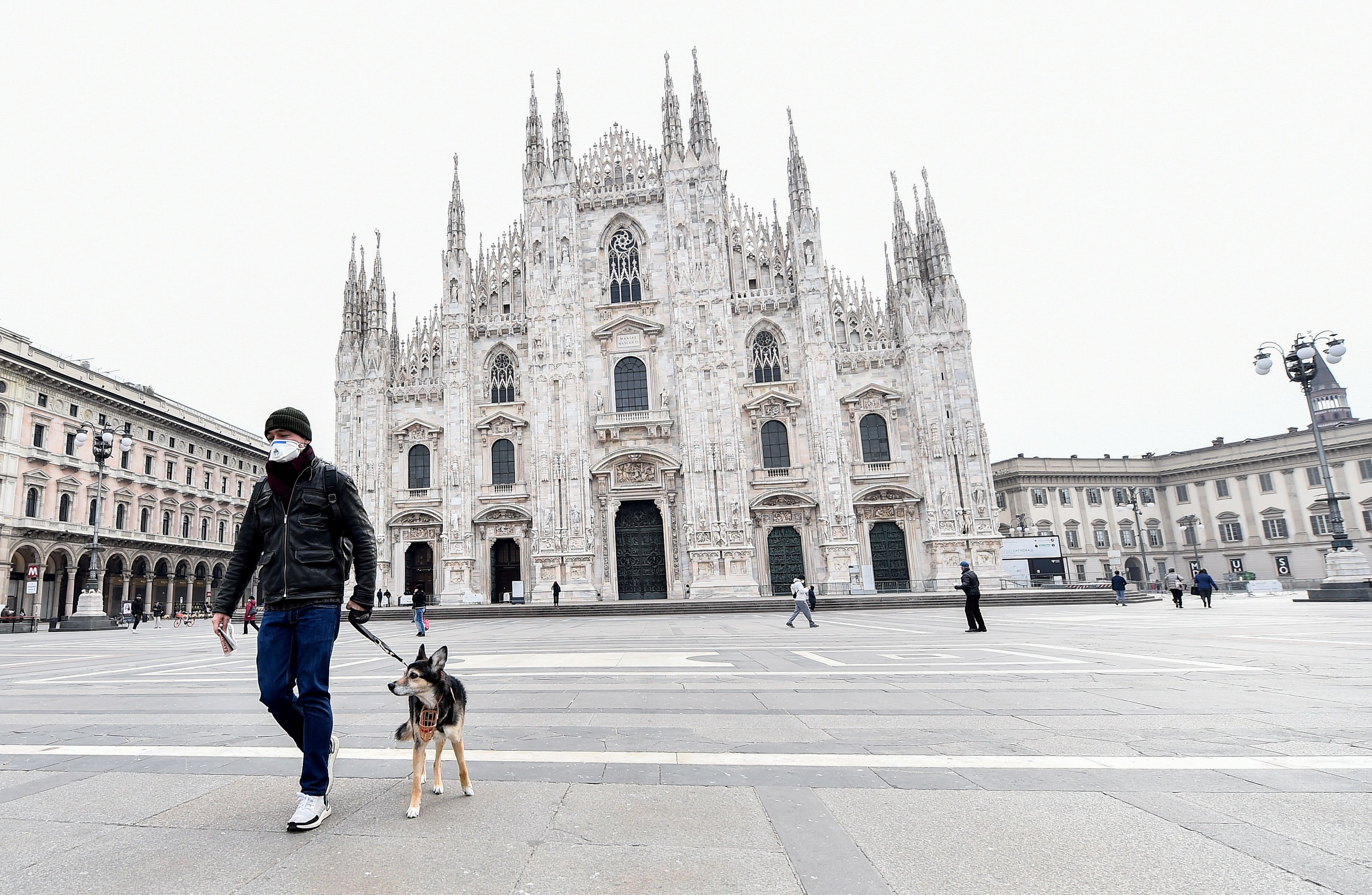 Un hombre pasea a su perro en la plaza del Duomo (Milán) durante la pandemia de coronavirus.