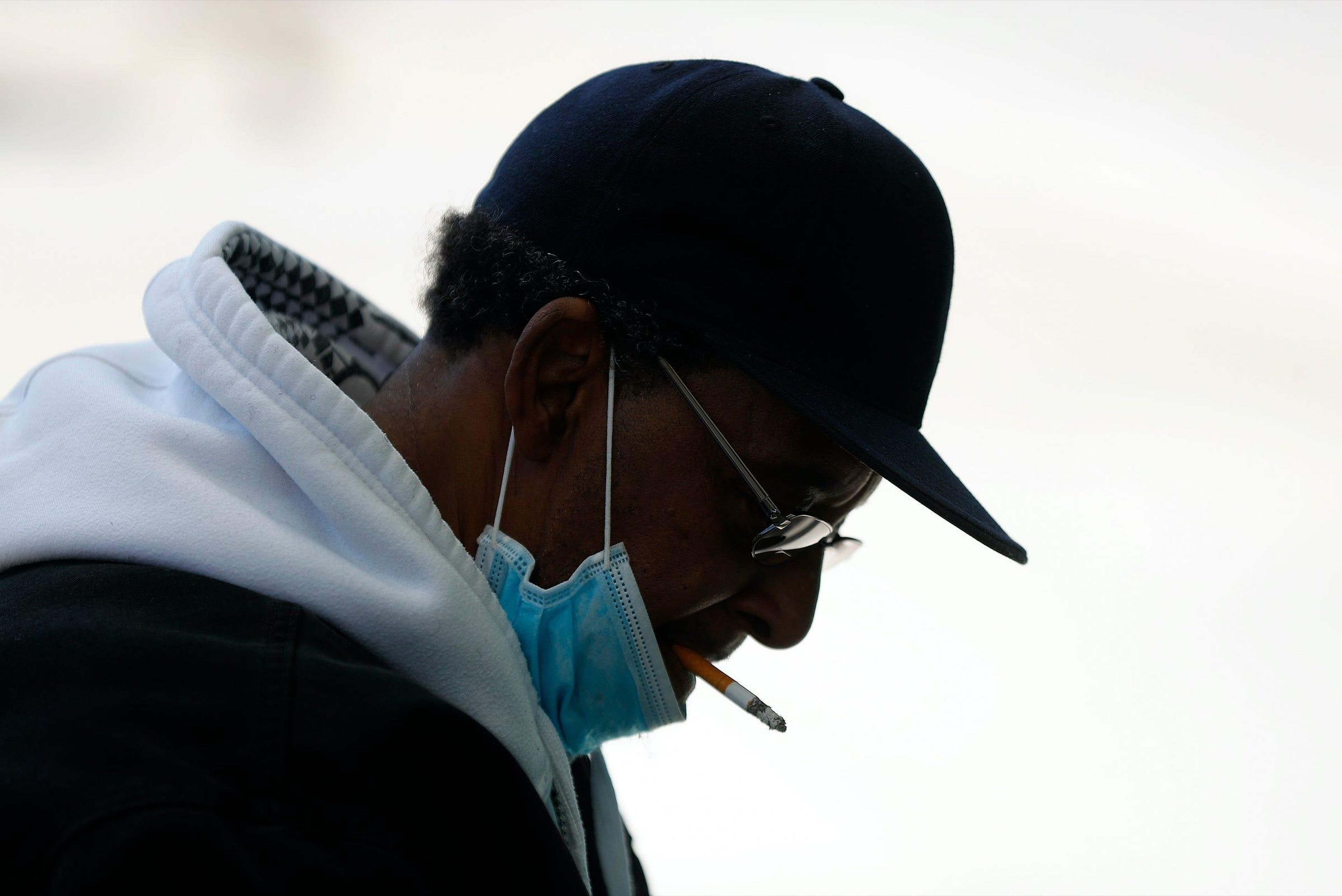 A man smokes a cigarette while wearing a protective mask while waiting for a bus in Detroit, Wednesday, April 8, 2020.