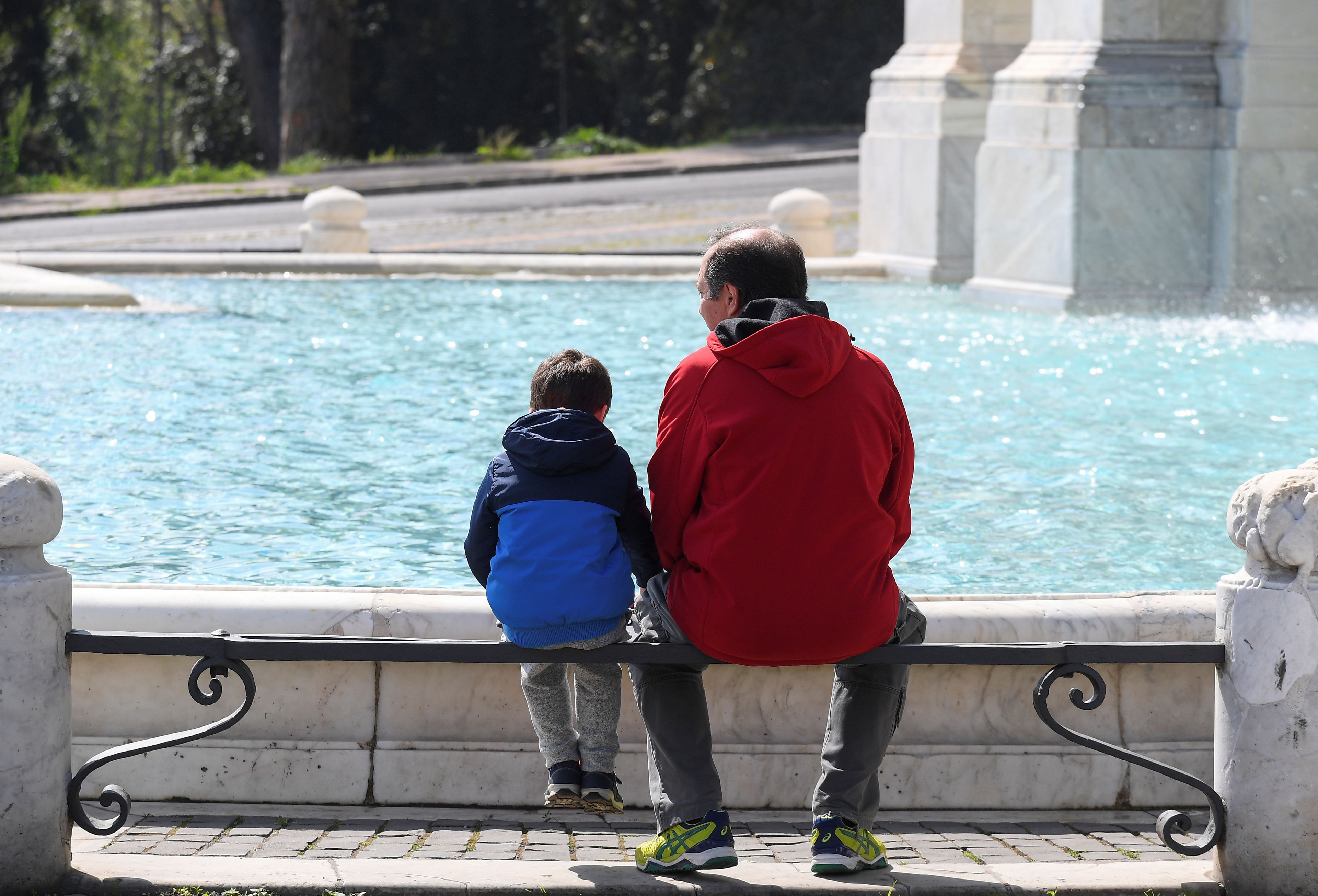 Un padre y un hijo sentados mirando una fuente.