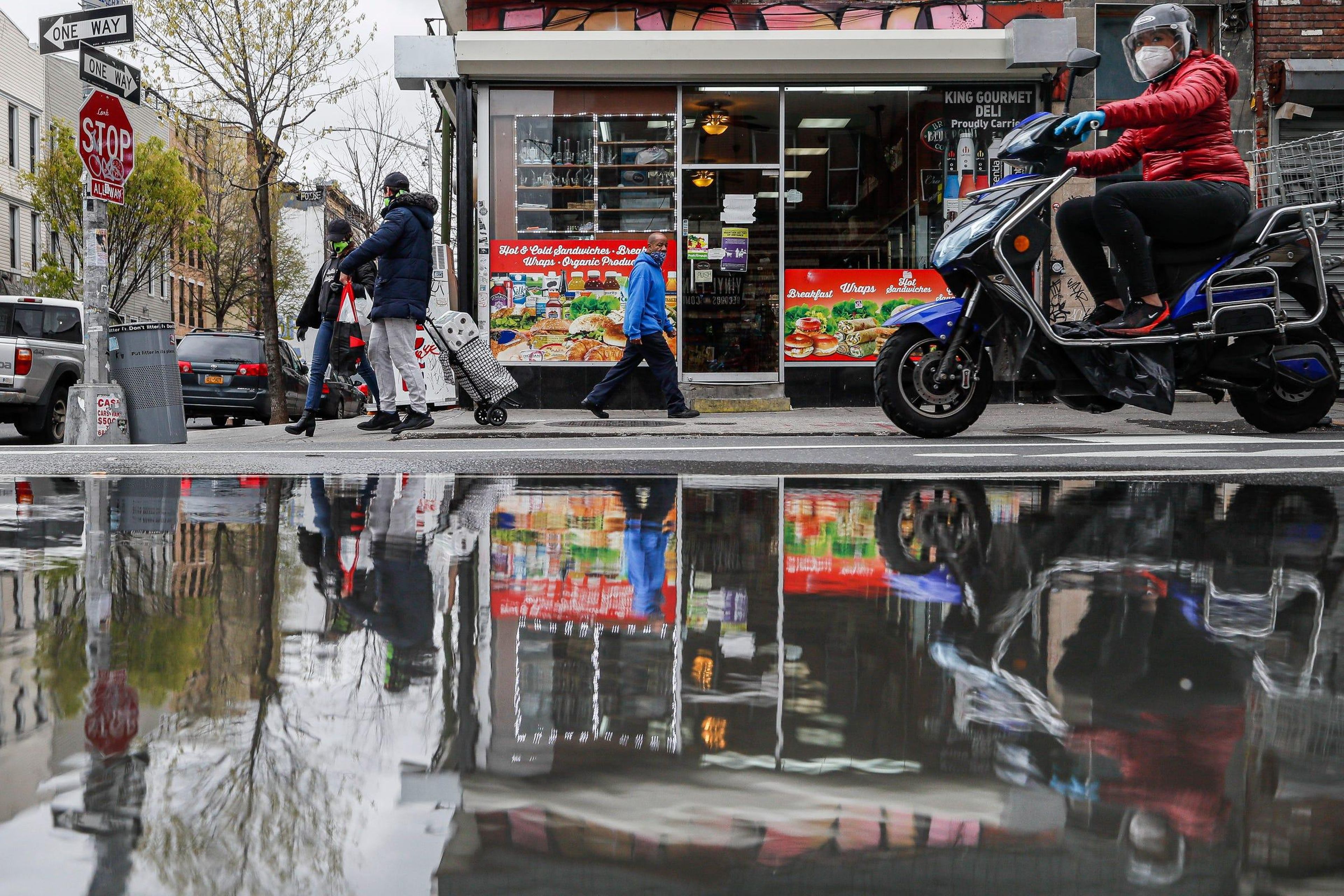 Pedestrians and motorists wear personal protective equipment as they pass a small grocery that is one of the few businesses open on the street in New York. (AP Photo/John Minchillo)