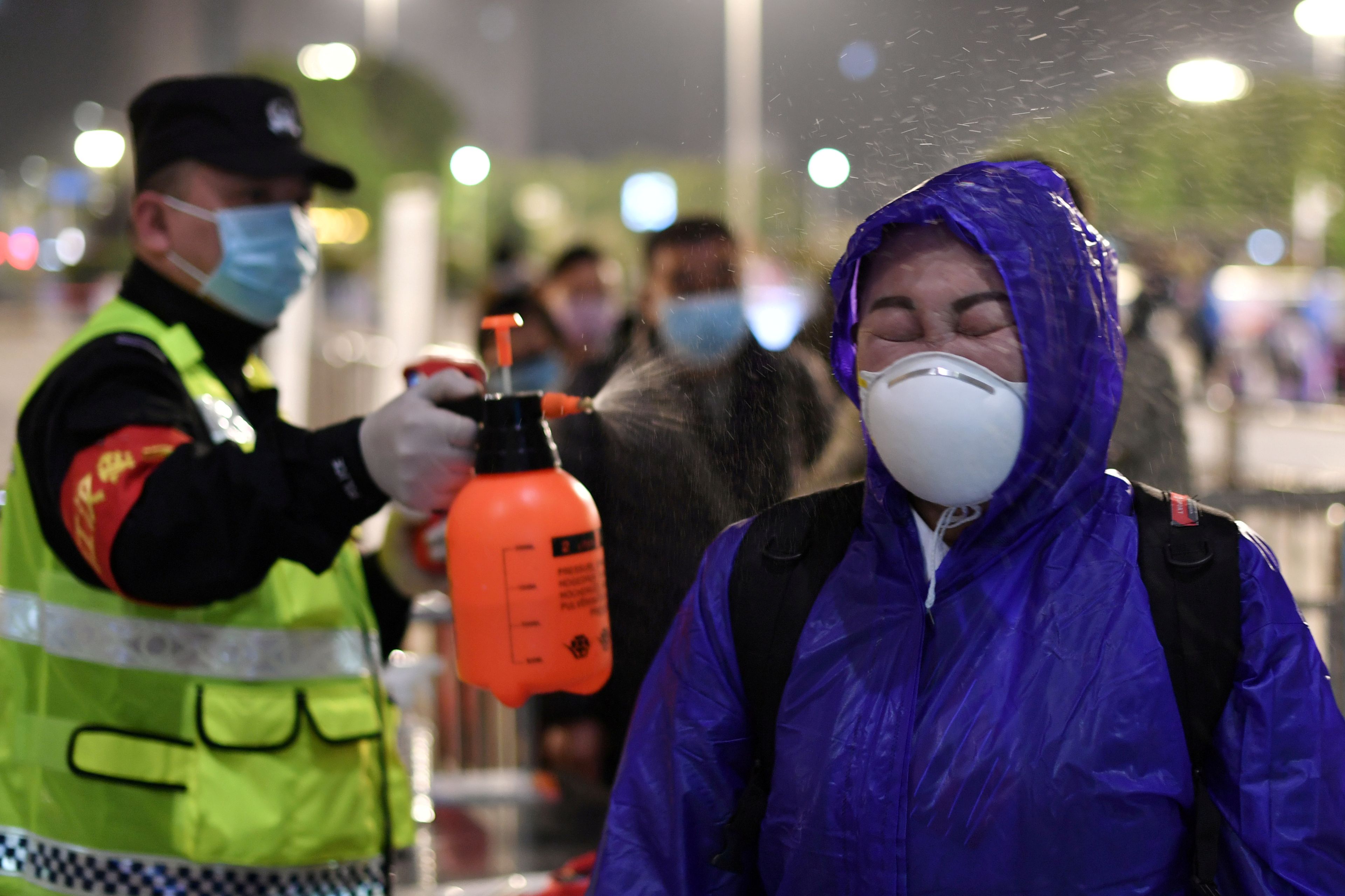 Un policía rocía con desinfectante a un viajero en la estación de trenes de Wuhan