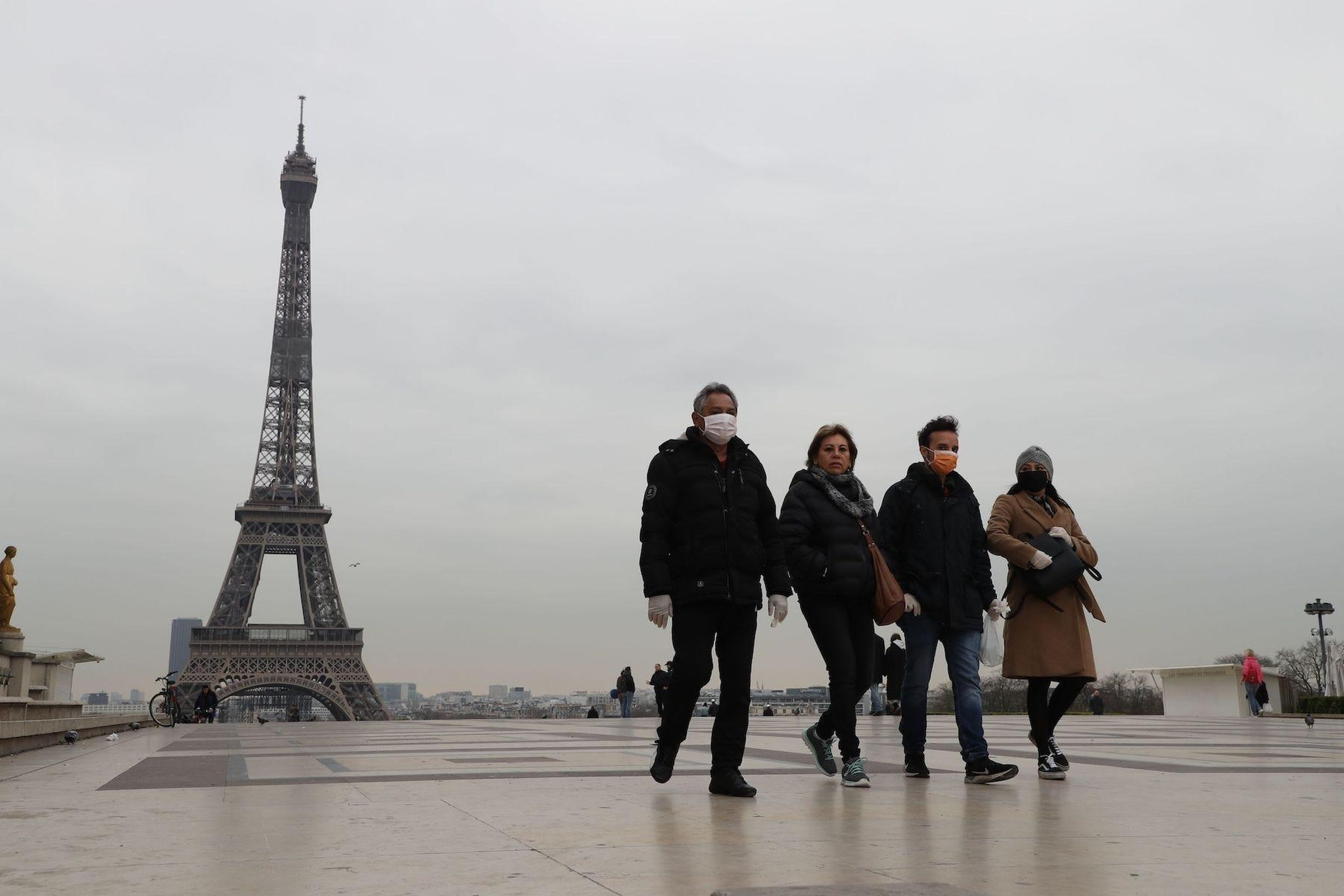 Turistas con mascarillas protectoras frente a la Torre Eiffel de París, el 17 de marzo de 2020, unas horas antes de que entre en vigor el confinamiento.