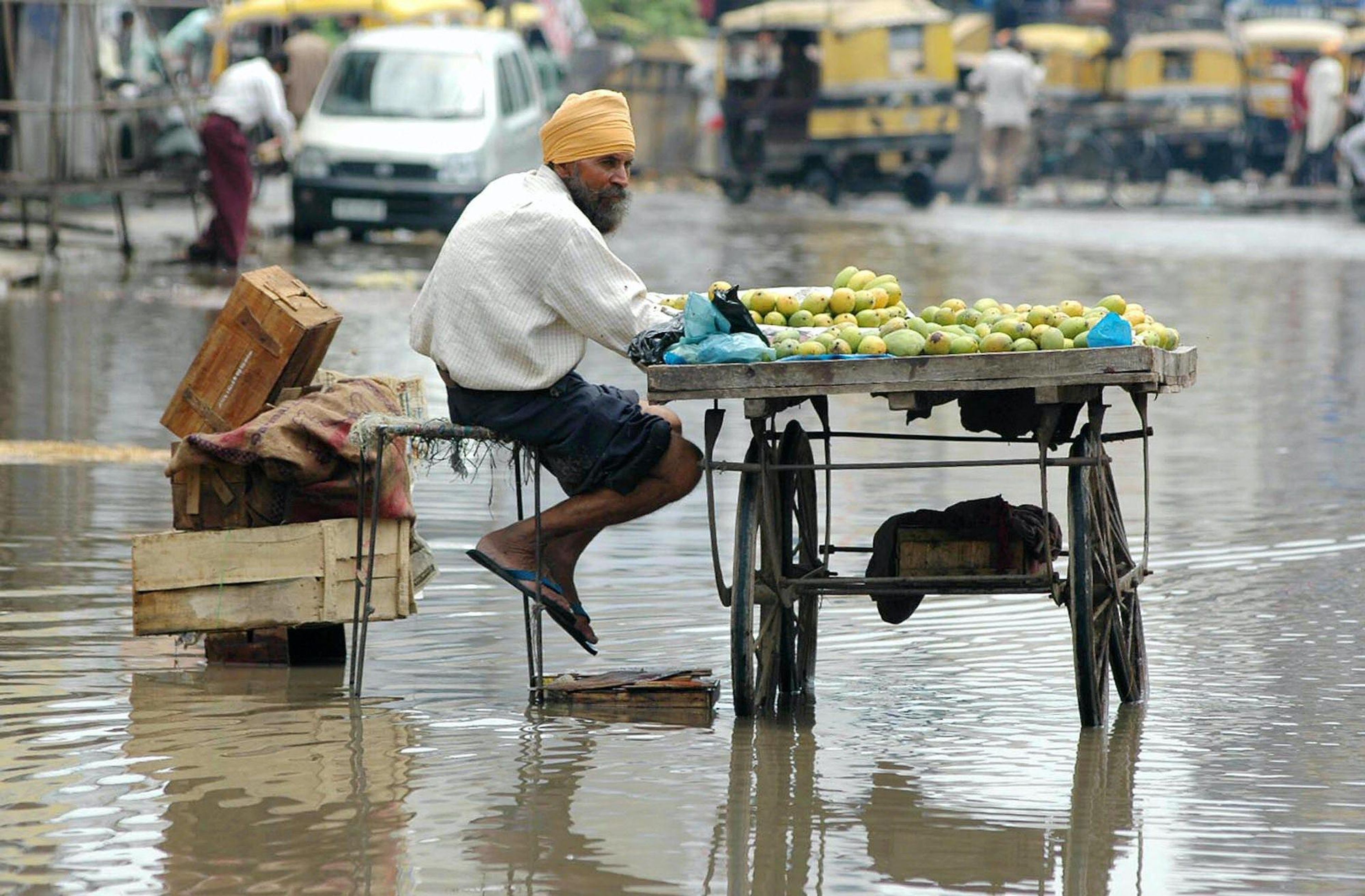 An Indian fruit vendor, Bhupinder Sethi sits on a flooded street as he waits for customers near the bus stand in Punjab.