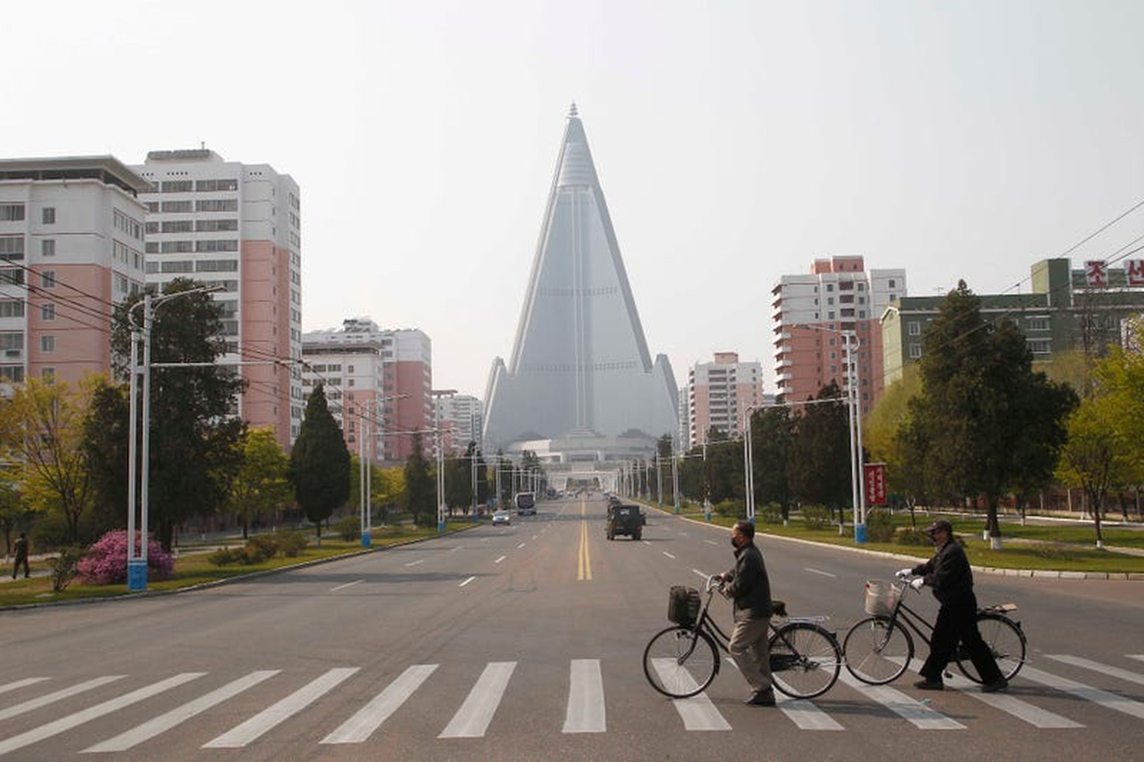 Personas con máscaras cruzan una calle frente al Hotel Ryugyong en Pyongyang, Corea del Norte, el martes 28 de abril de 2020.