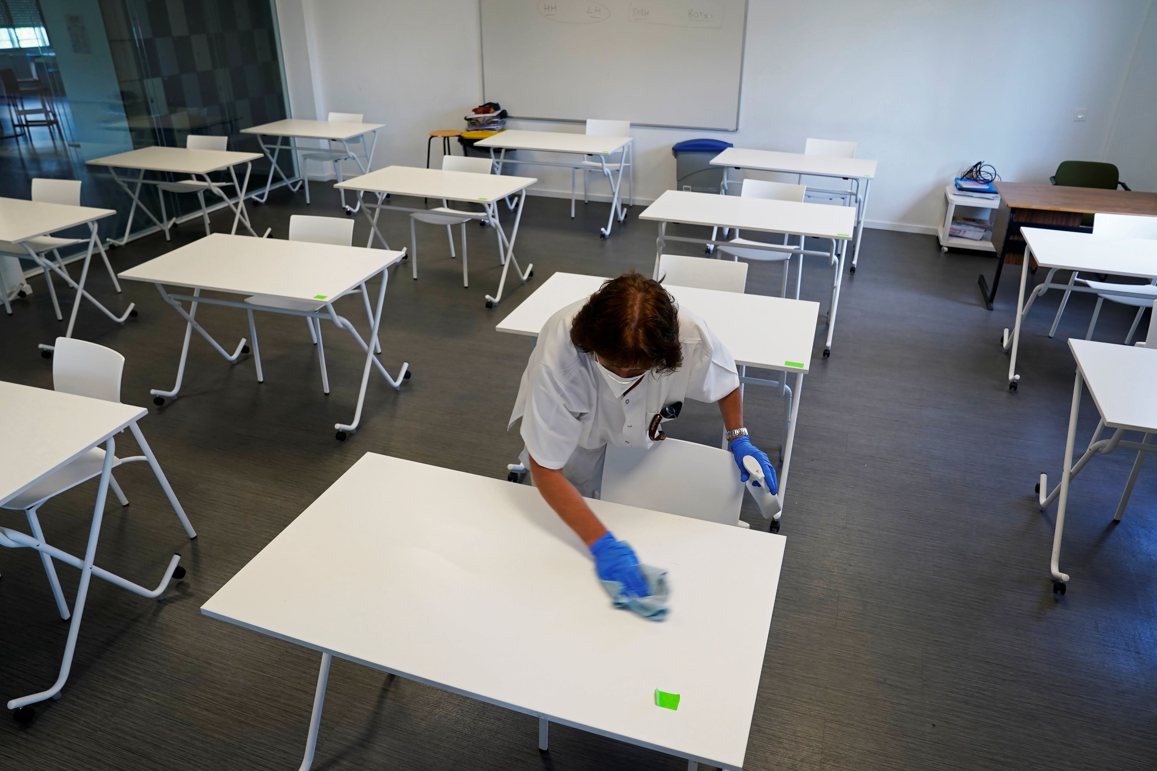Una limpiadora desinfecta las mesas de un aula en un colegio de San Sebastián, que reabrirá la semana que viene tras la pandemia del coronavirus