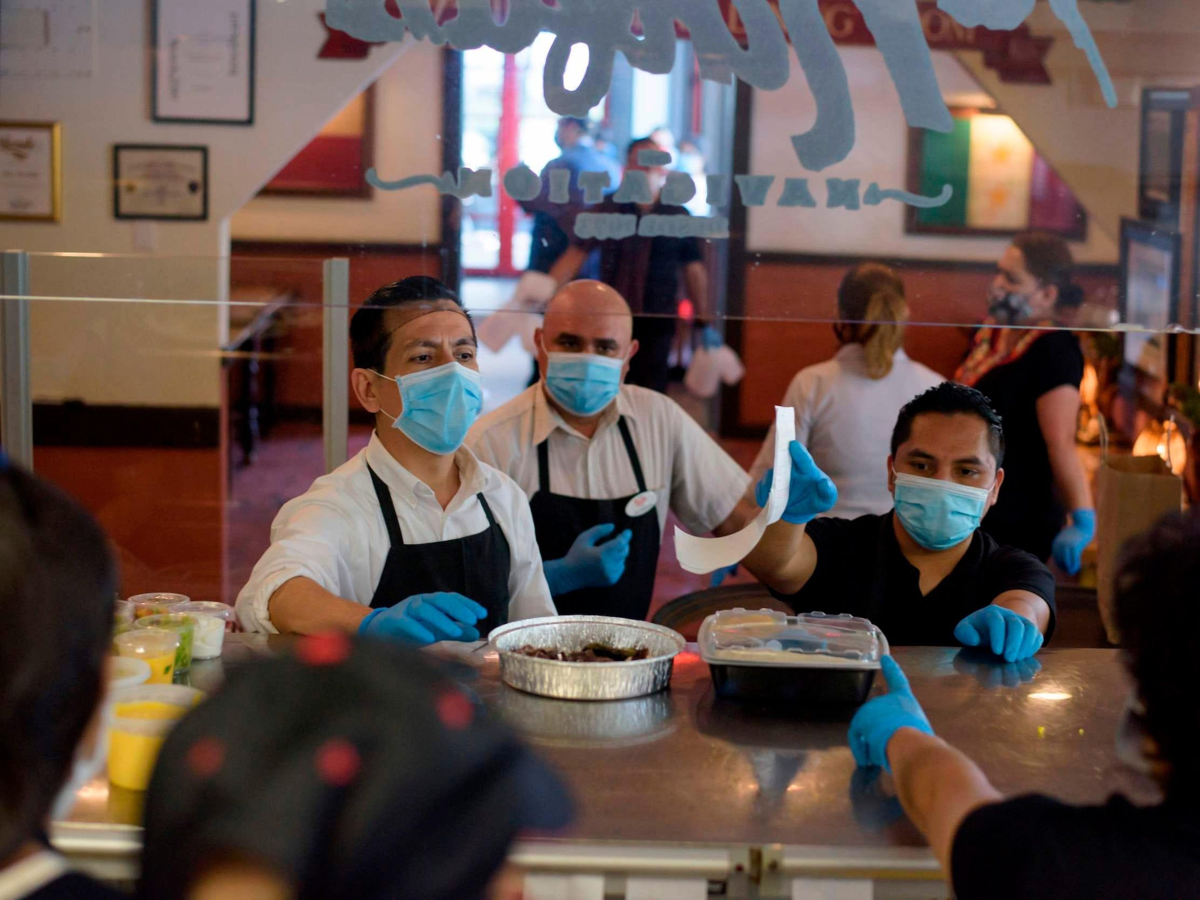 Servers wearing gloves and masks get takeout orders from the kitchen at a restaurant in Houston, Texas, on May 1.