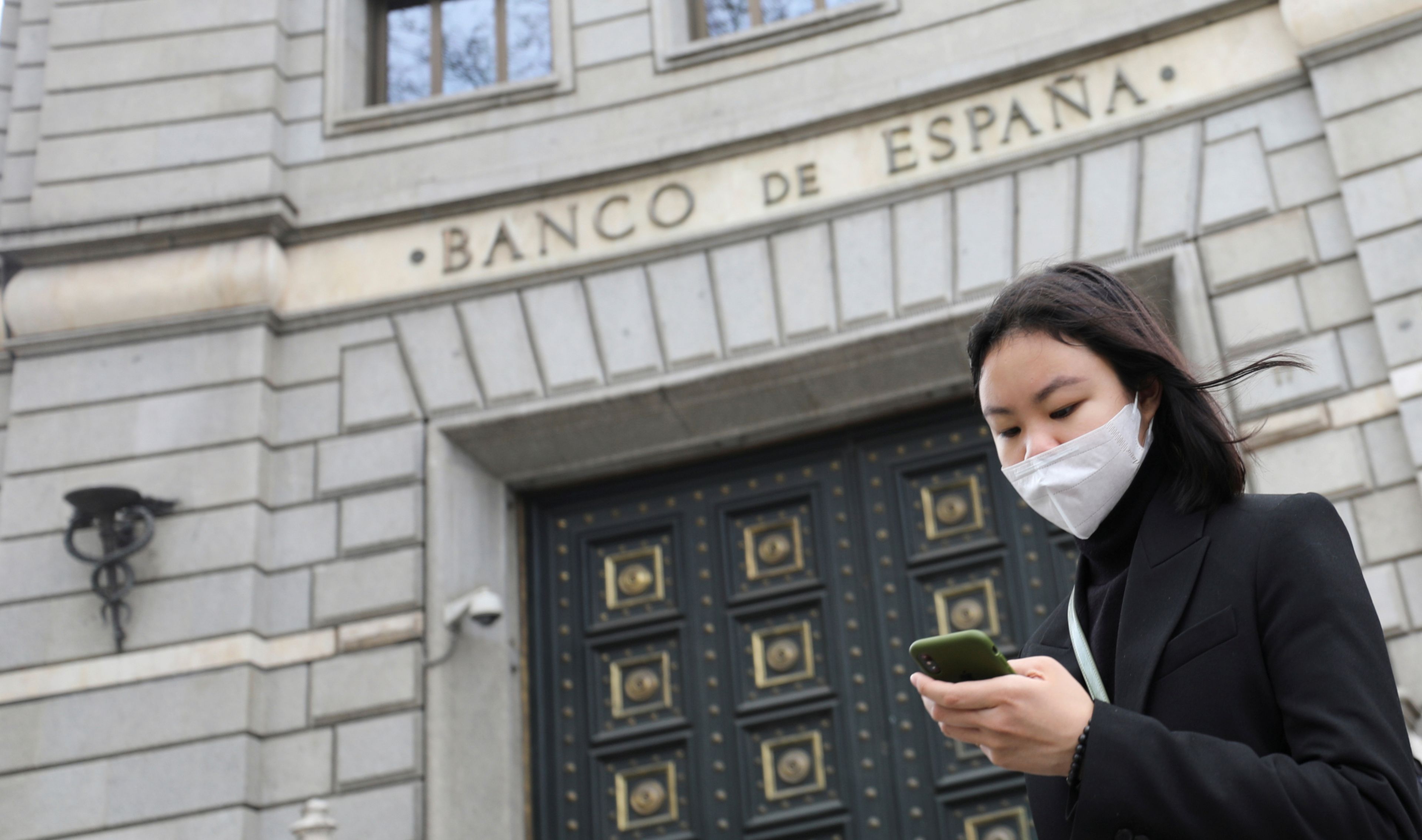 Una mujer con mascarilla pasa ante la sede del Banco de España en Madrid