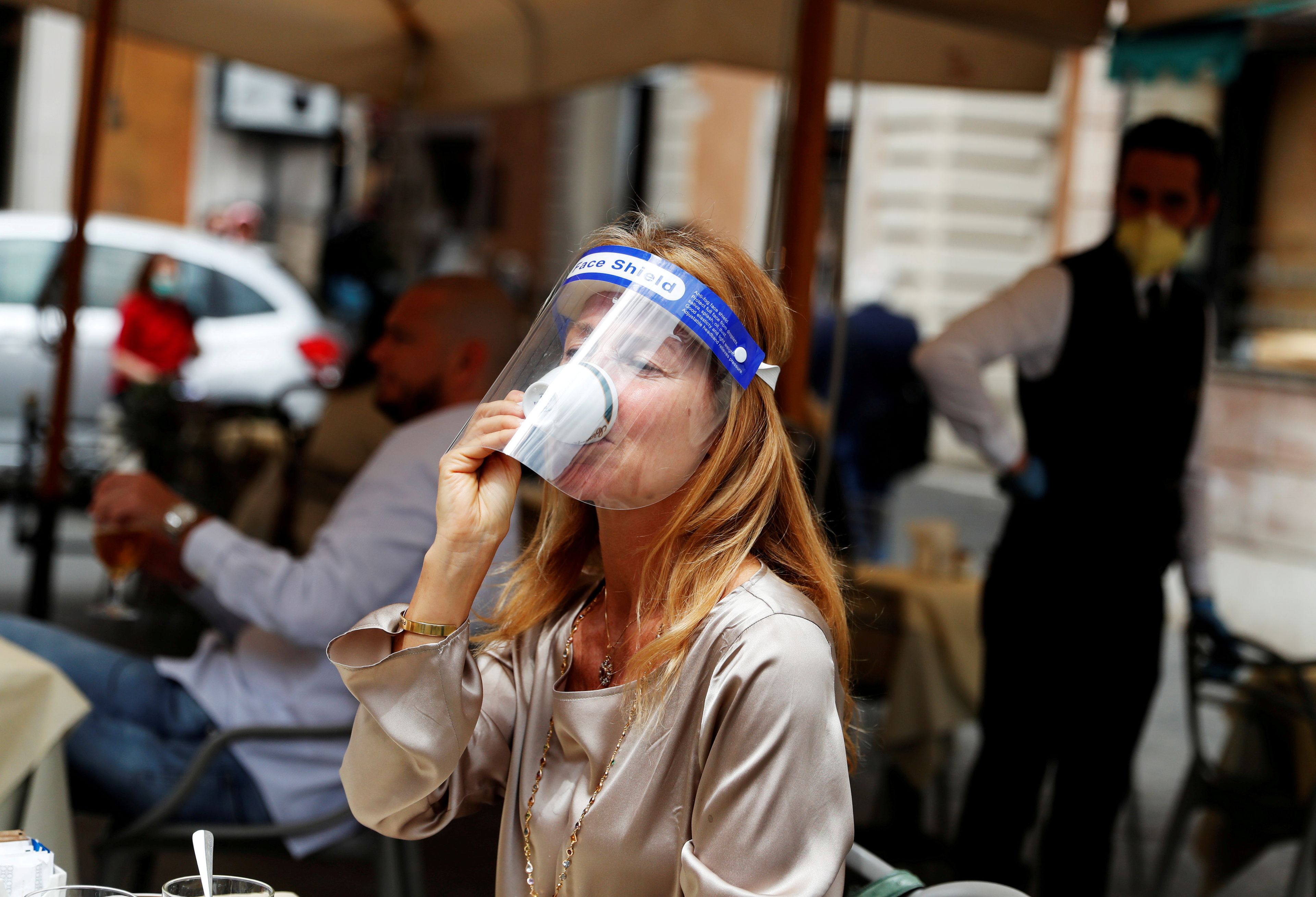 Una mujer con una pantalla facial se toma un café en Roma tras el desconfinamiento de algunas medidas en Italia