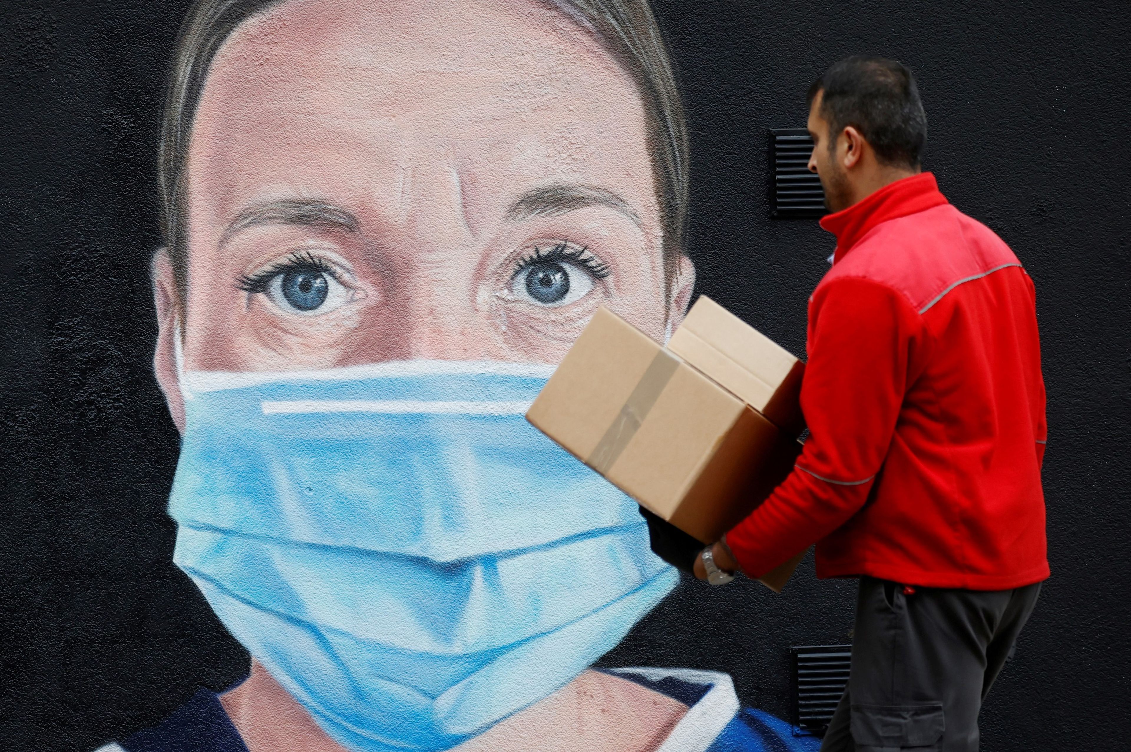 Un repartido pasa por delante de un mural con motivo de la pandemia del coronavirus