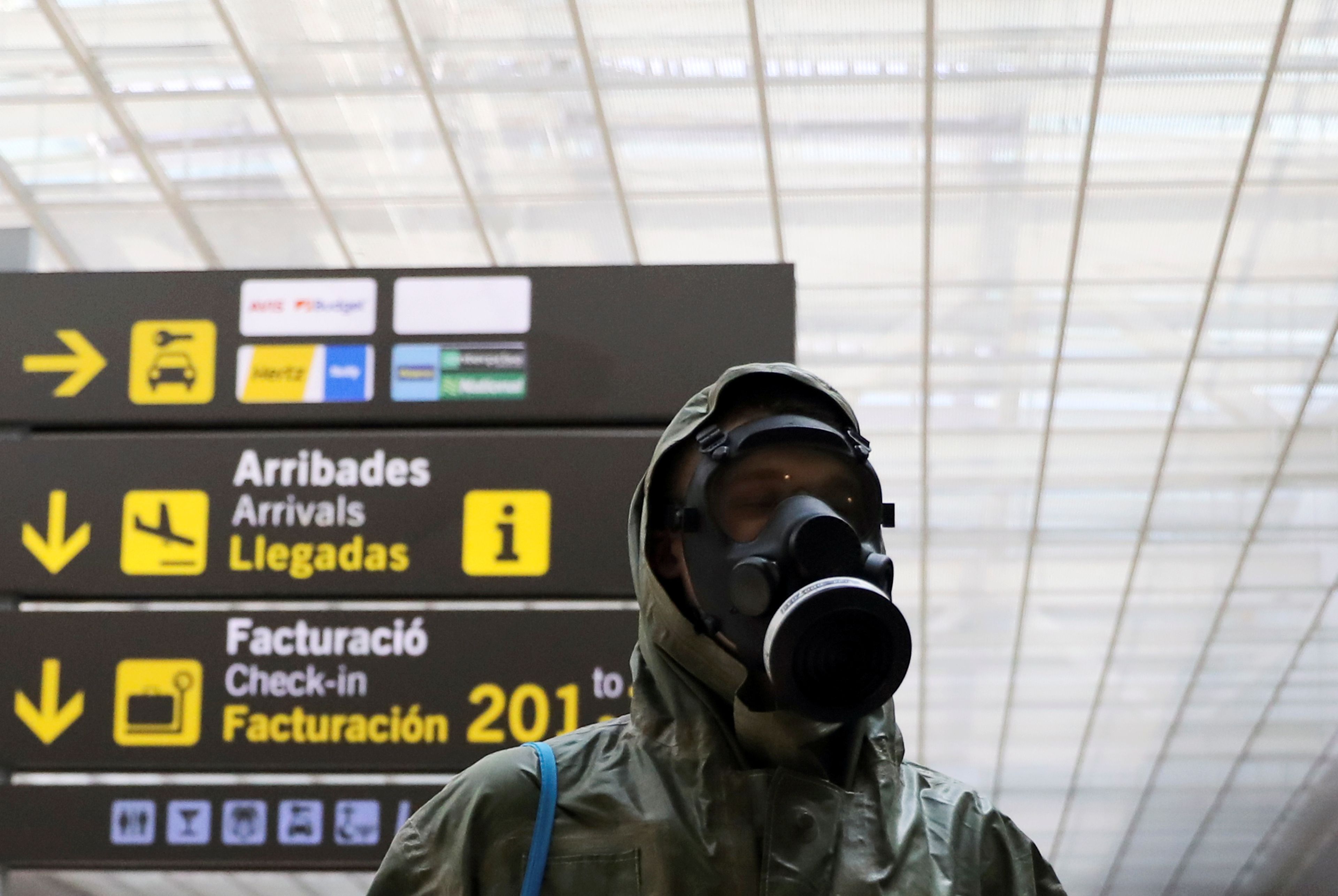 Un viajero equipado con máscara de gas y traje protector en el aeropuerto de El Prato durante el confinamiento por el coronavirus