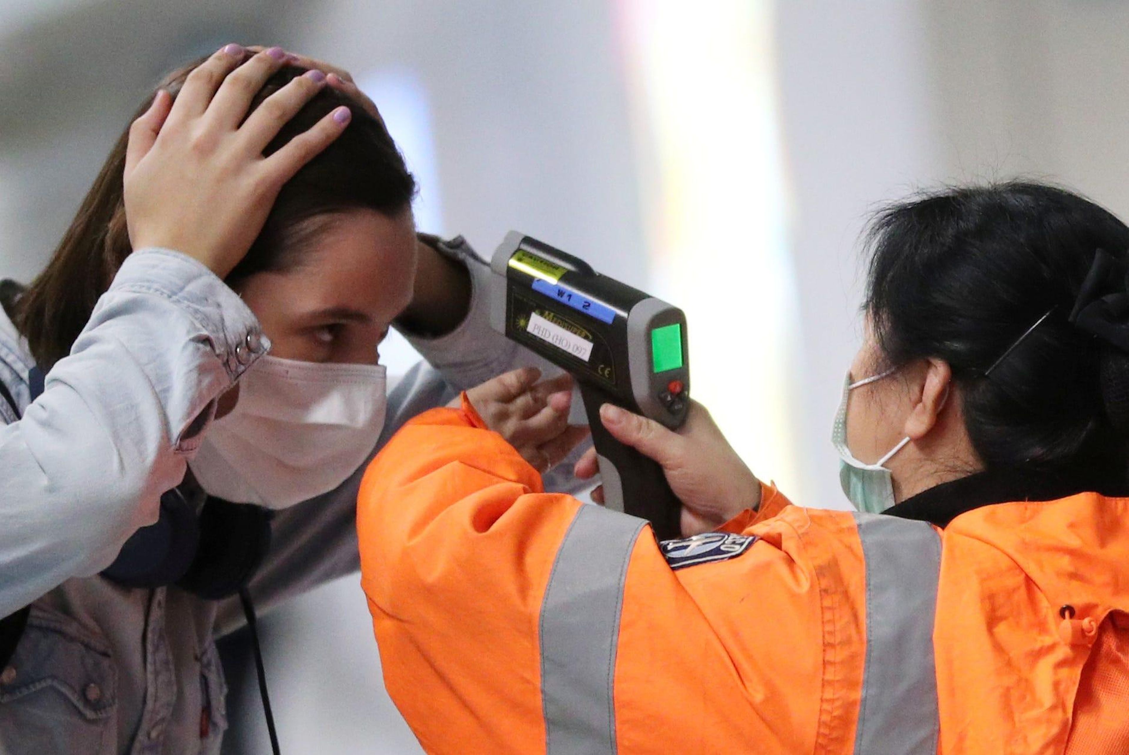 Un trabajador verifica la temperatura de un pasajero que llega al aeropuerto internacional de Hong Kong con un termómetro infrarrojo en febrero de 2020