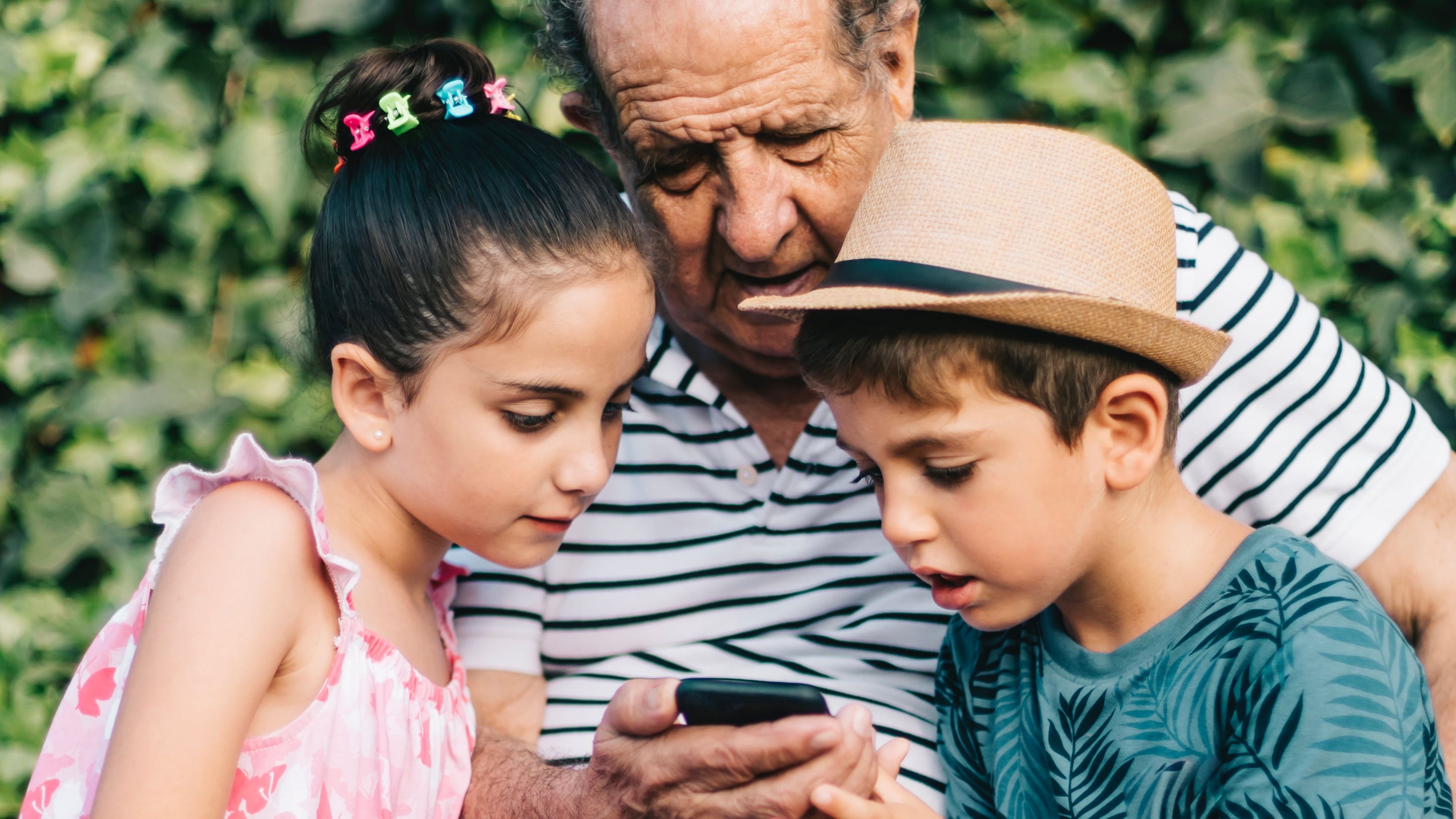 Un abuelo mira el móvil con sus dos nietos.