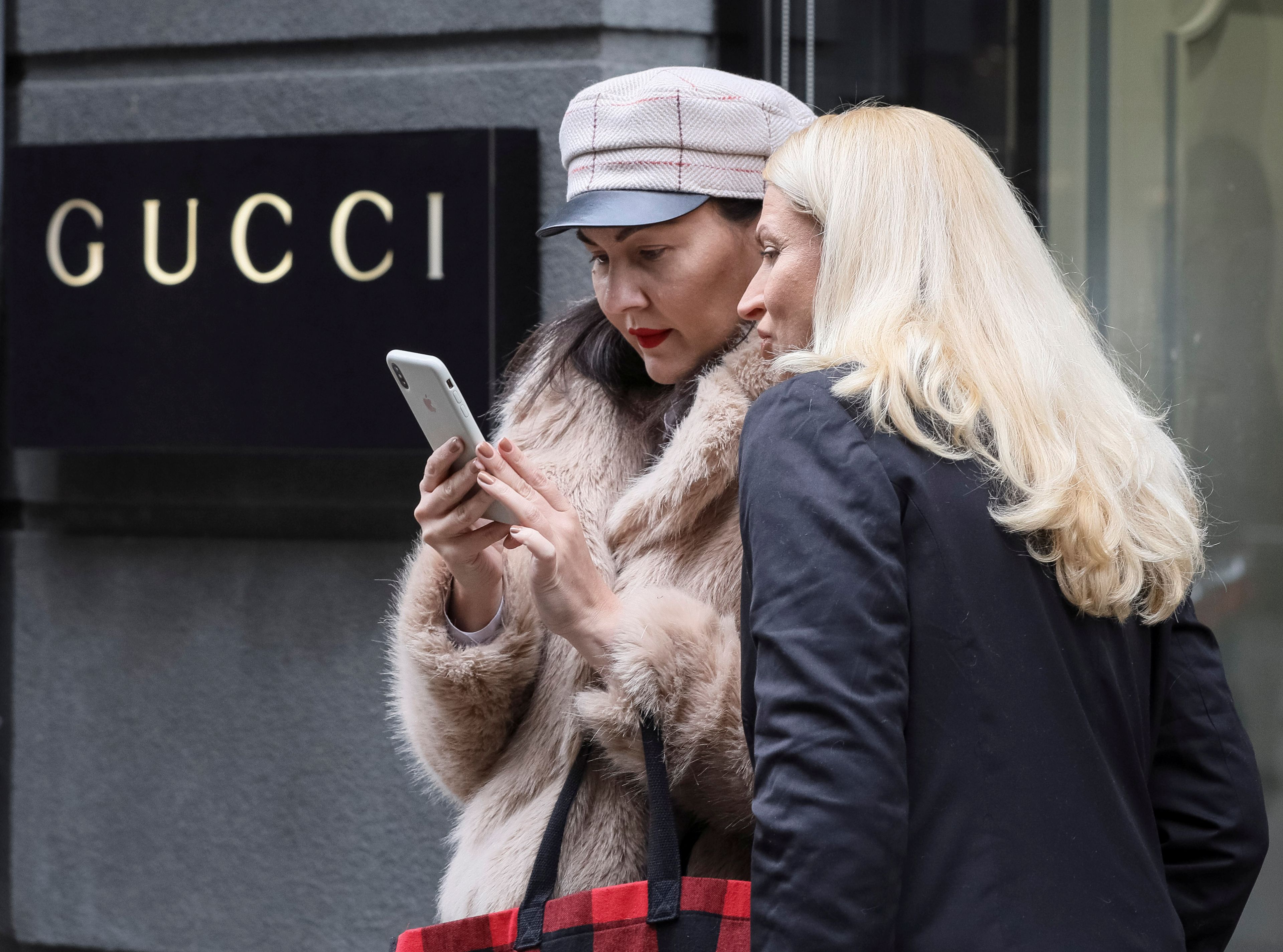 Dos mujeres miran un móvil frente a un escaparate de Gucci