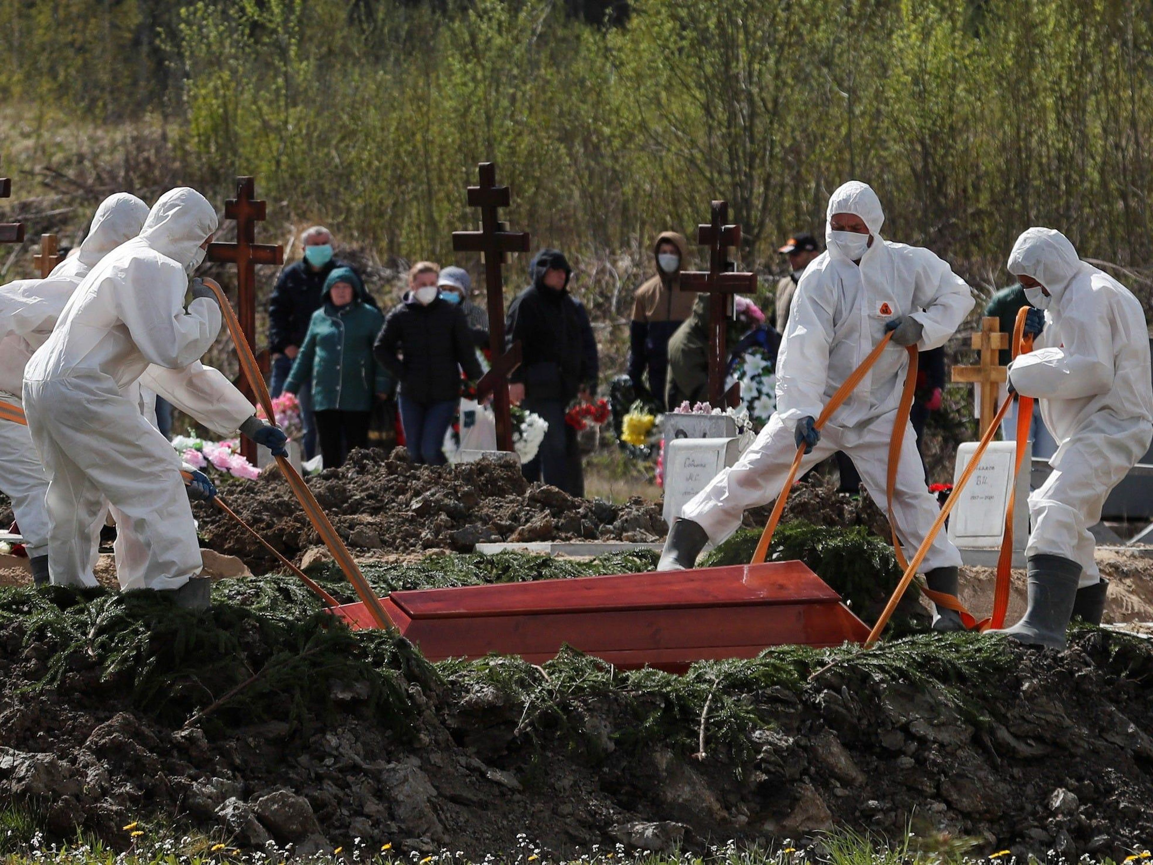 Excavadores de tumbas bajan el ataúd de una persona que supuestamente murió de un coronavirus, mientras los enlutados con máscaras se reúnen en un cementerio en las afueras de San Petersburgo, Rusia, el 13 de mayo de 2020.