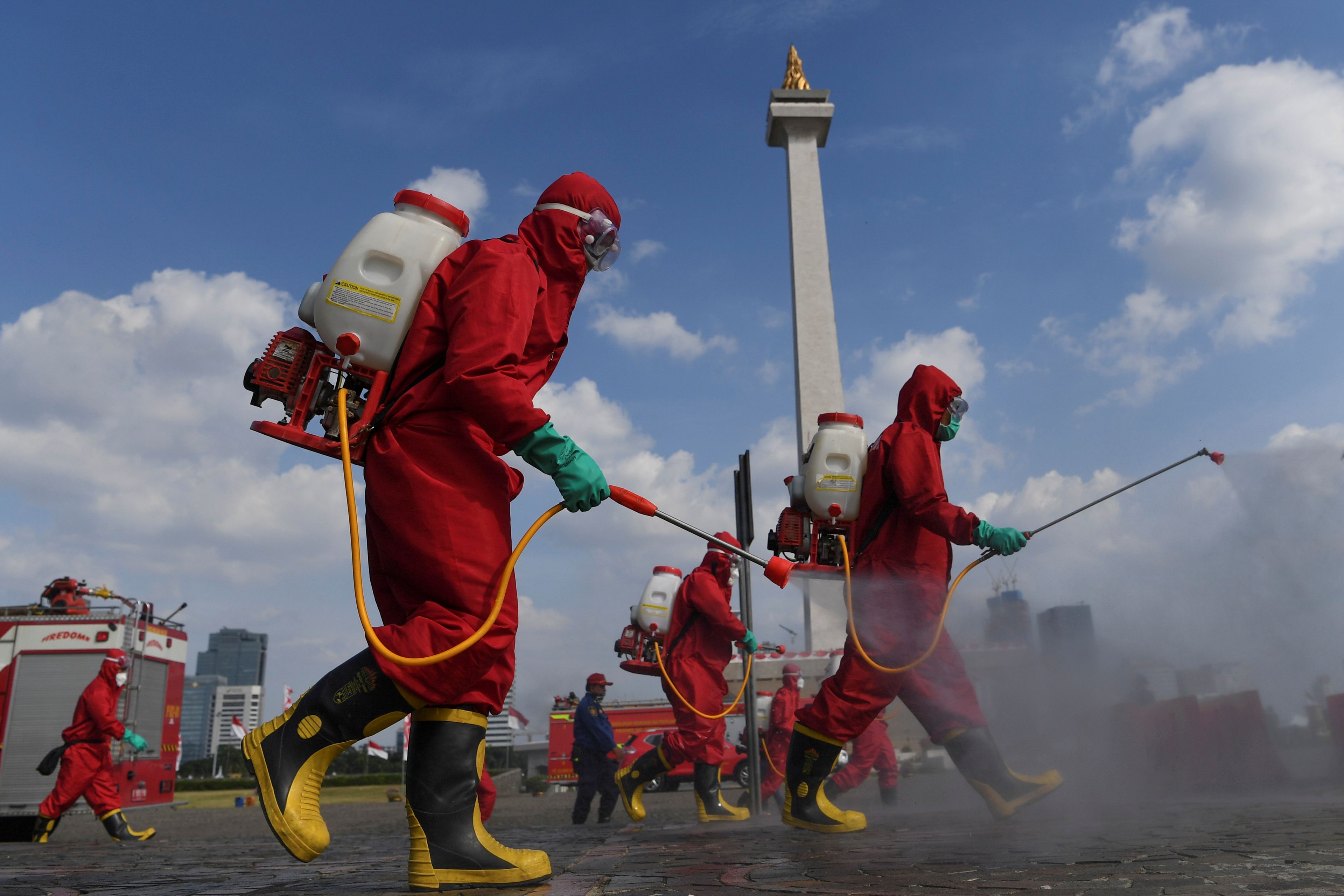 Un grupo de bomberos con trajes protectores desinfecta una zona turística en Yakarta pare frenar la propagación del coronavirus.