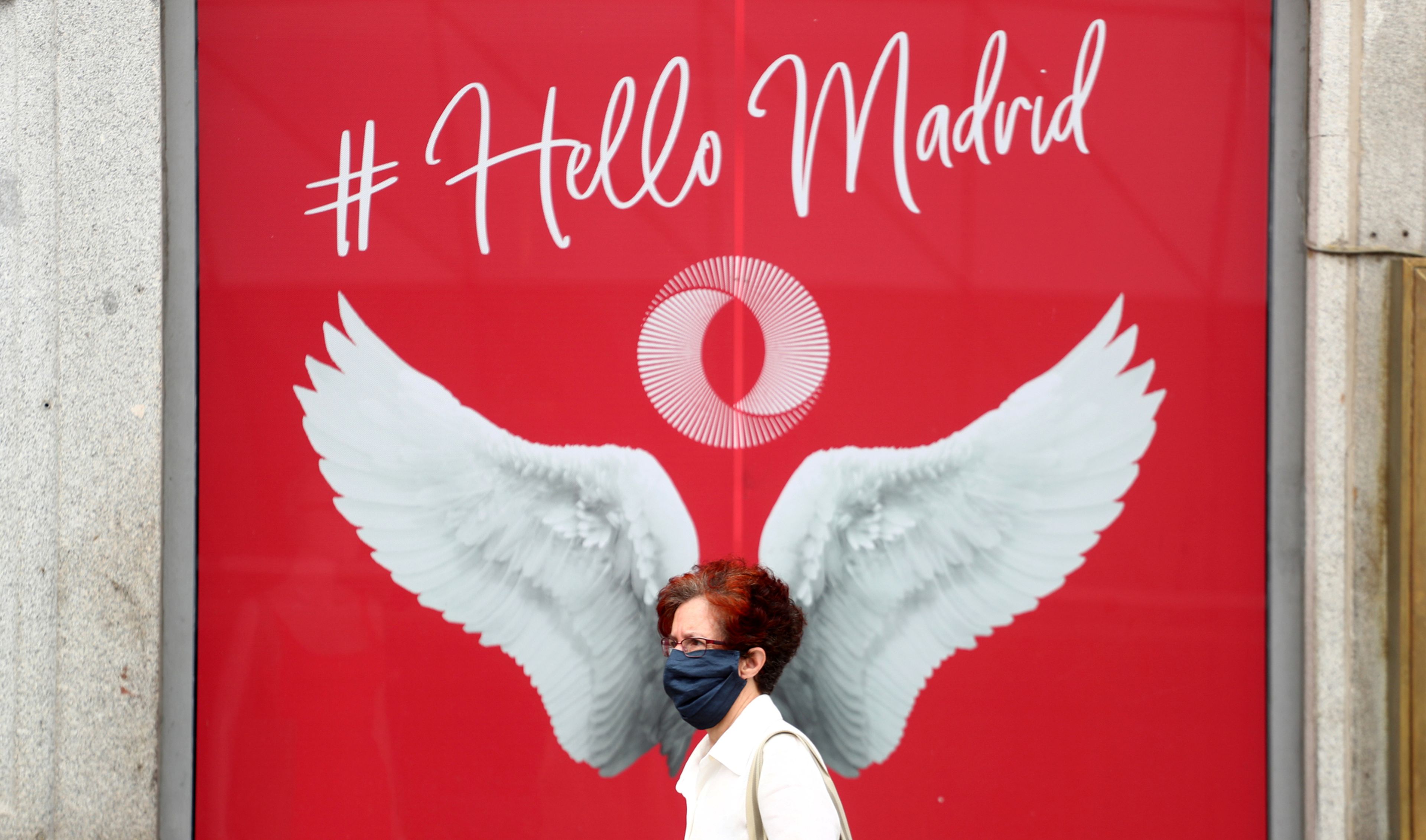 Una mujer con mascarilla pasa ante un anuncio en una zona turística de Madrid