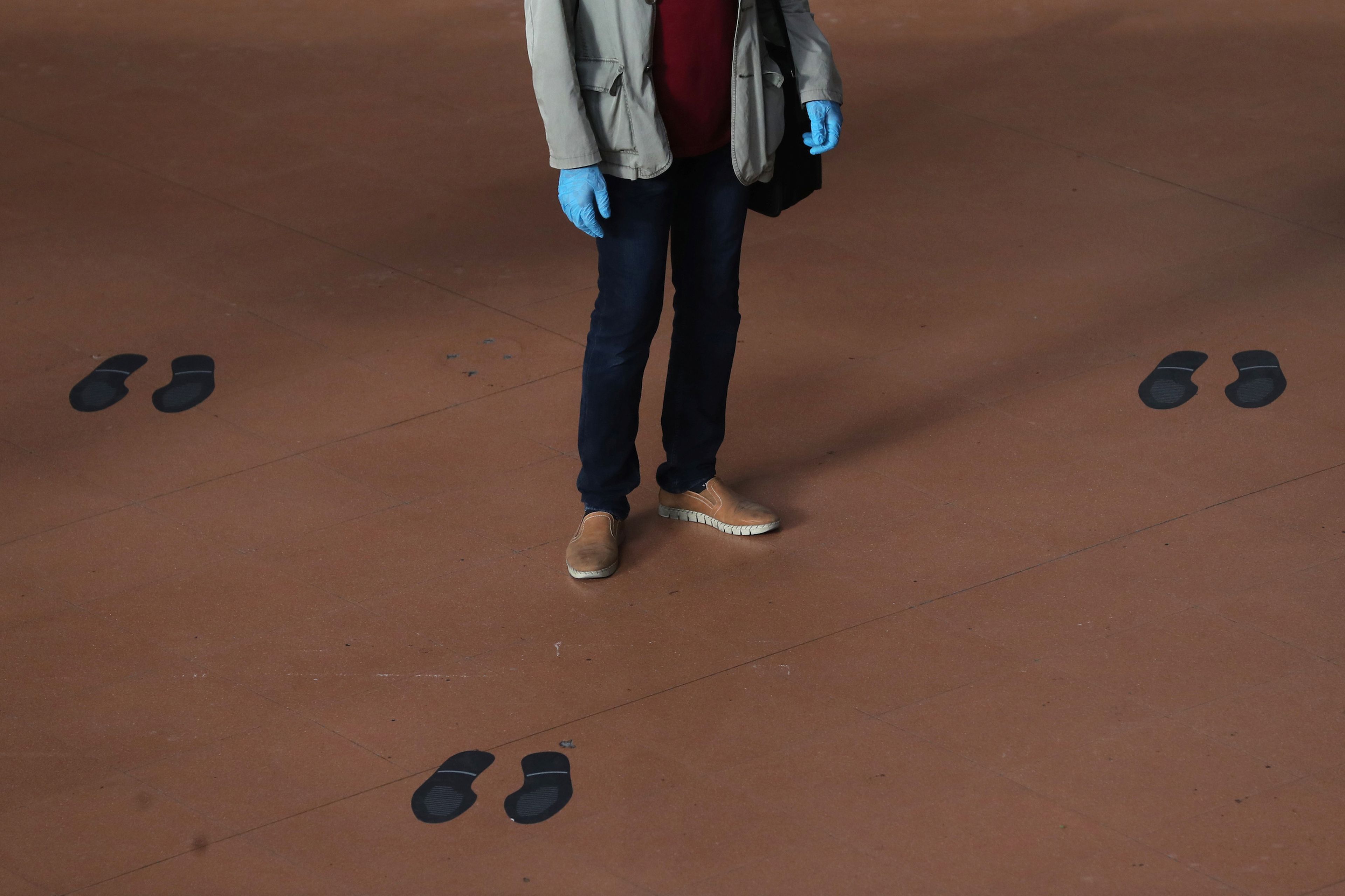 Un viajero con guantes protectores se para en medio de las marcas de distanciamiento social en el piso de la estación de trenes de Atocha.