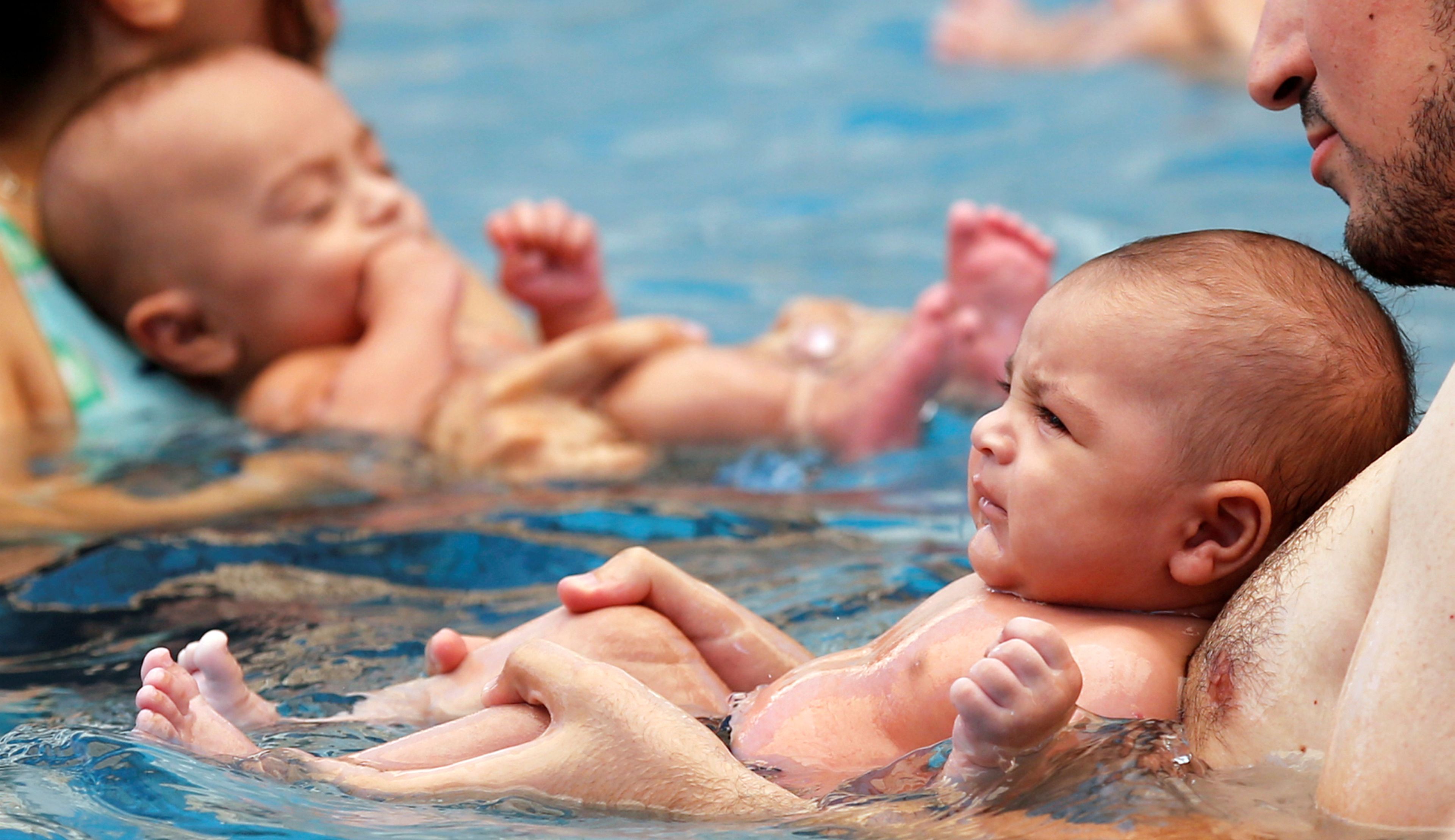 Bebés en manos de sus padres durante una clase de natación para neonatos