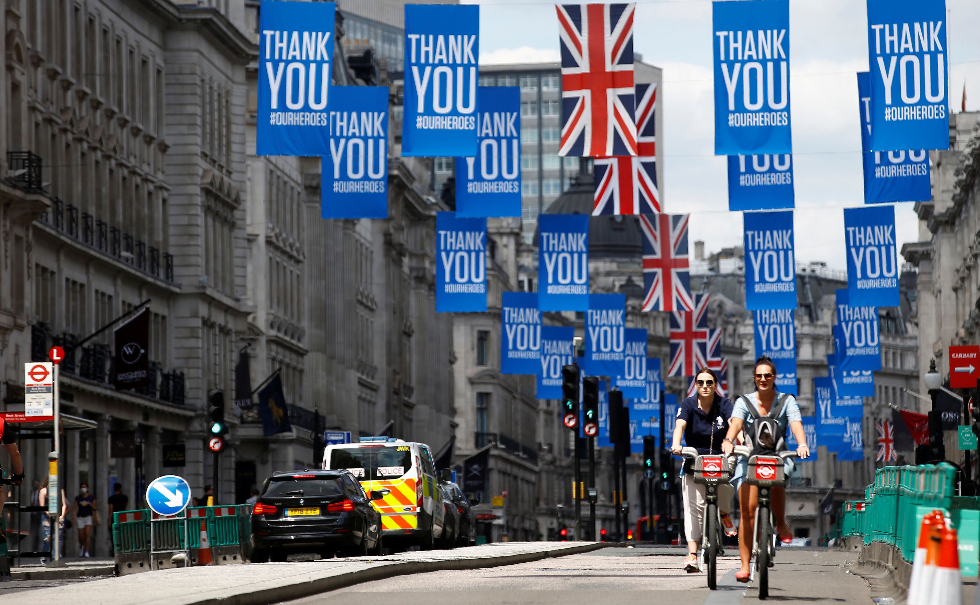 Ciclistas en Londres atraviesan una calle con carteles en agradecimiento por el comportamiento de la población durante la pandemia.