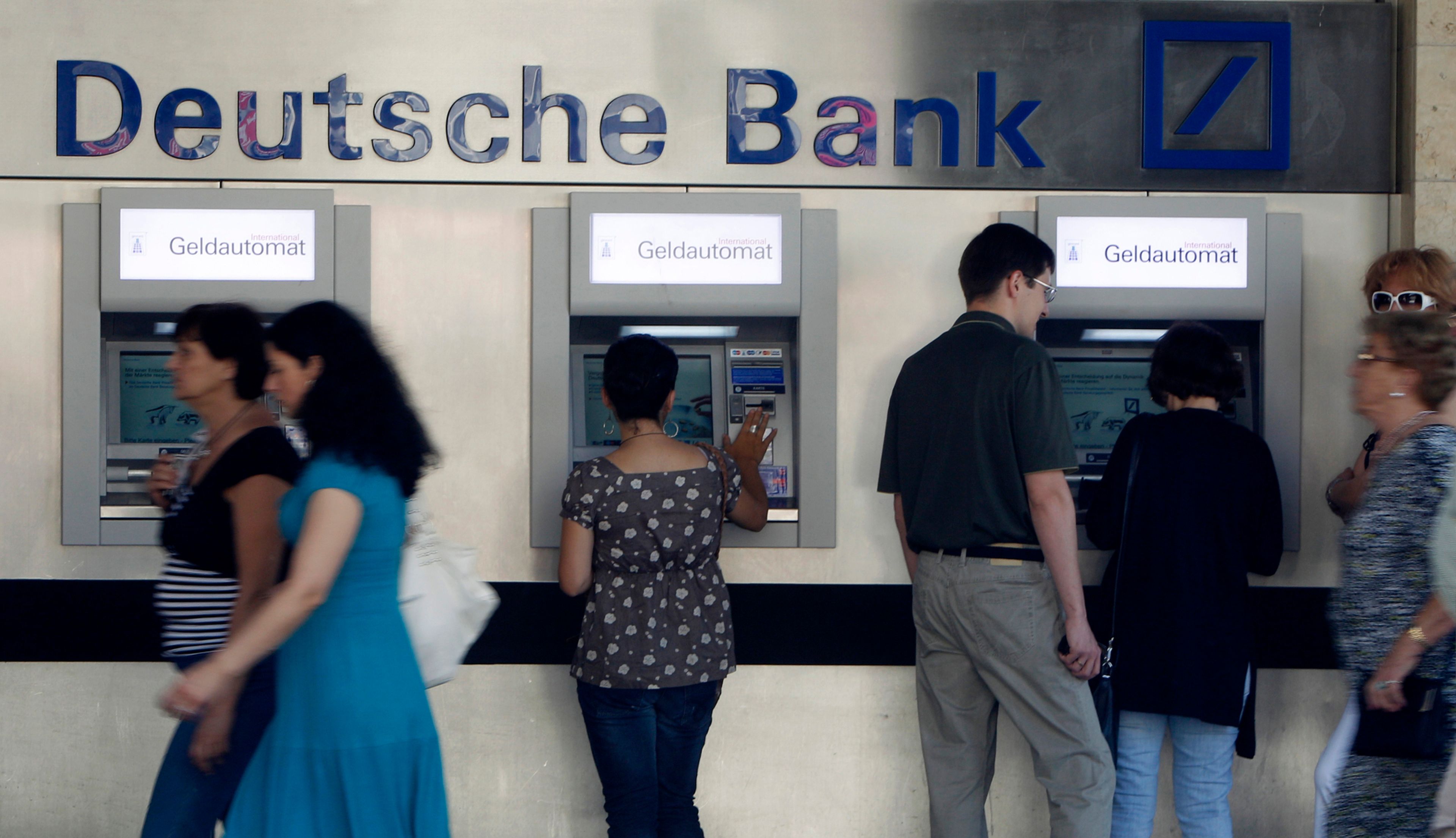 Clientes sacando dinero de cajeros automáticos en una sucursal de Deutsche Bank en Munich (Alemania)
